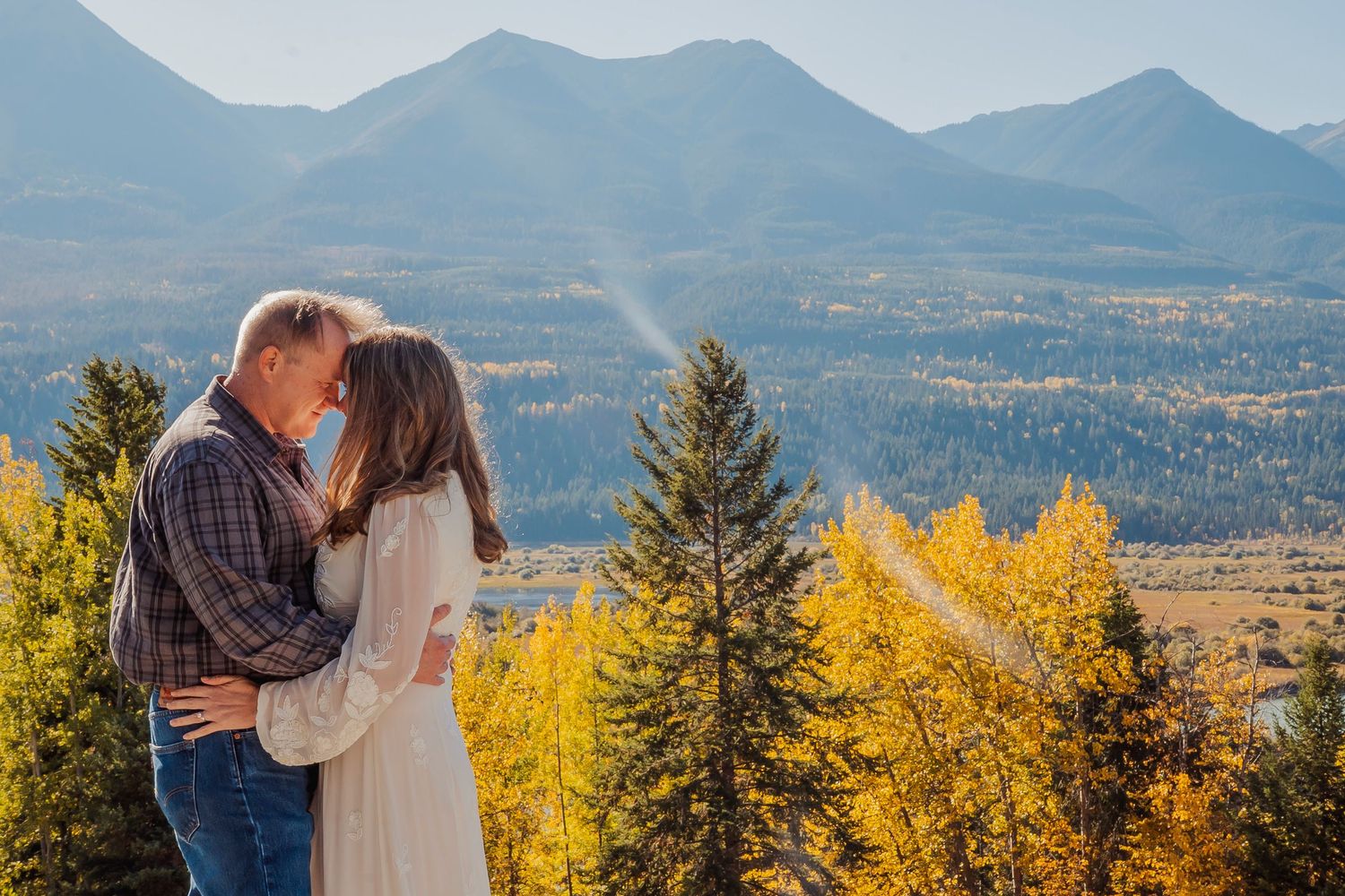 Couple embracing with mountain landscape and autumn foliage in background.