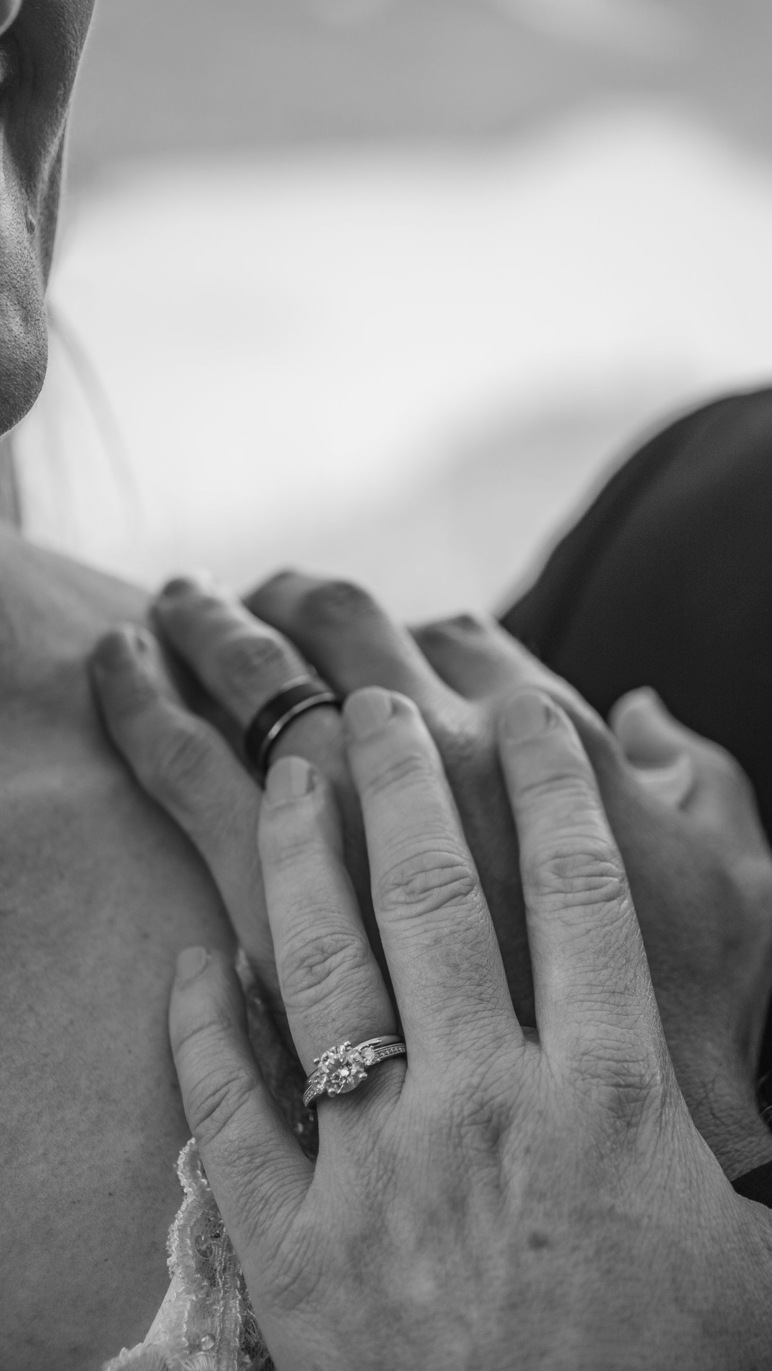 Black and white close-up of hands wearing engagement rings against a soft background.
