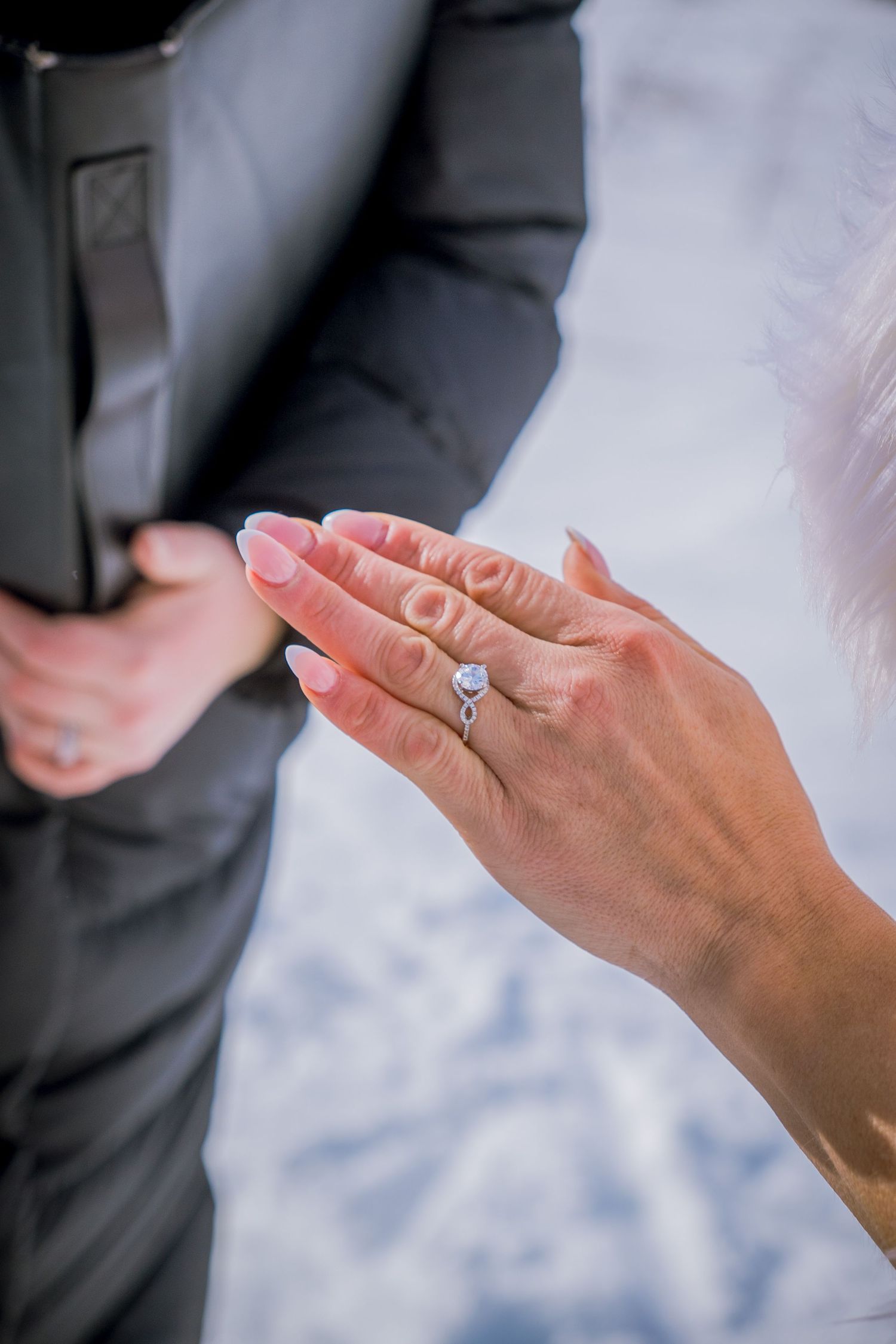 Close-up of hands showing off an engagement ring against a snowy winter backdrop.
