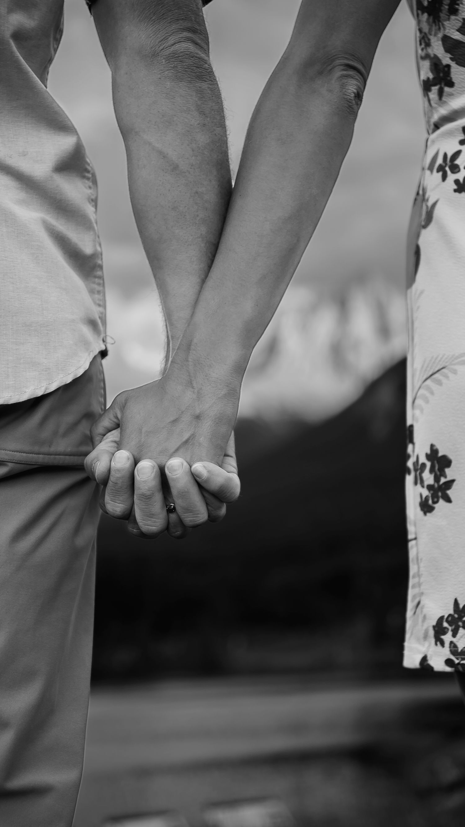 Black and white detail shot of couple holding hands against nature backdrop.