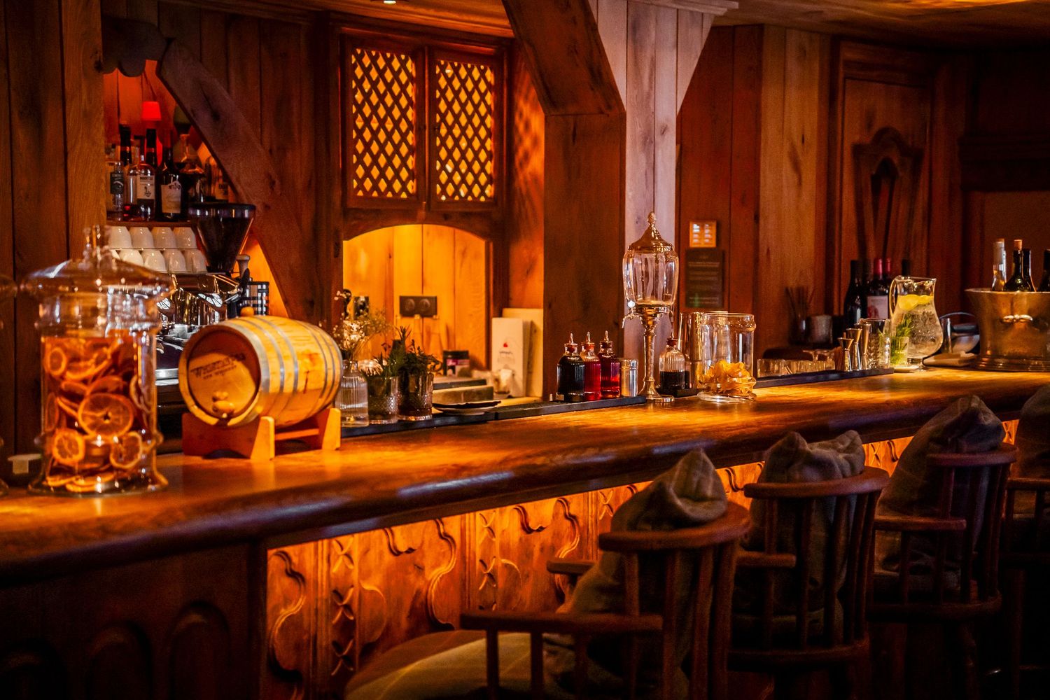 Cozy dimly lit bar interior with warm ambient lighting illuminating wooden counters and shelves stocked with bottles.