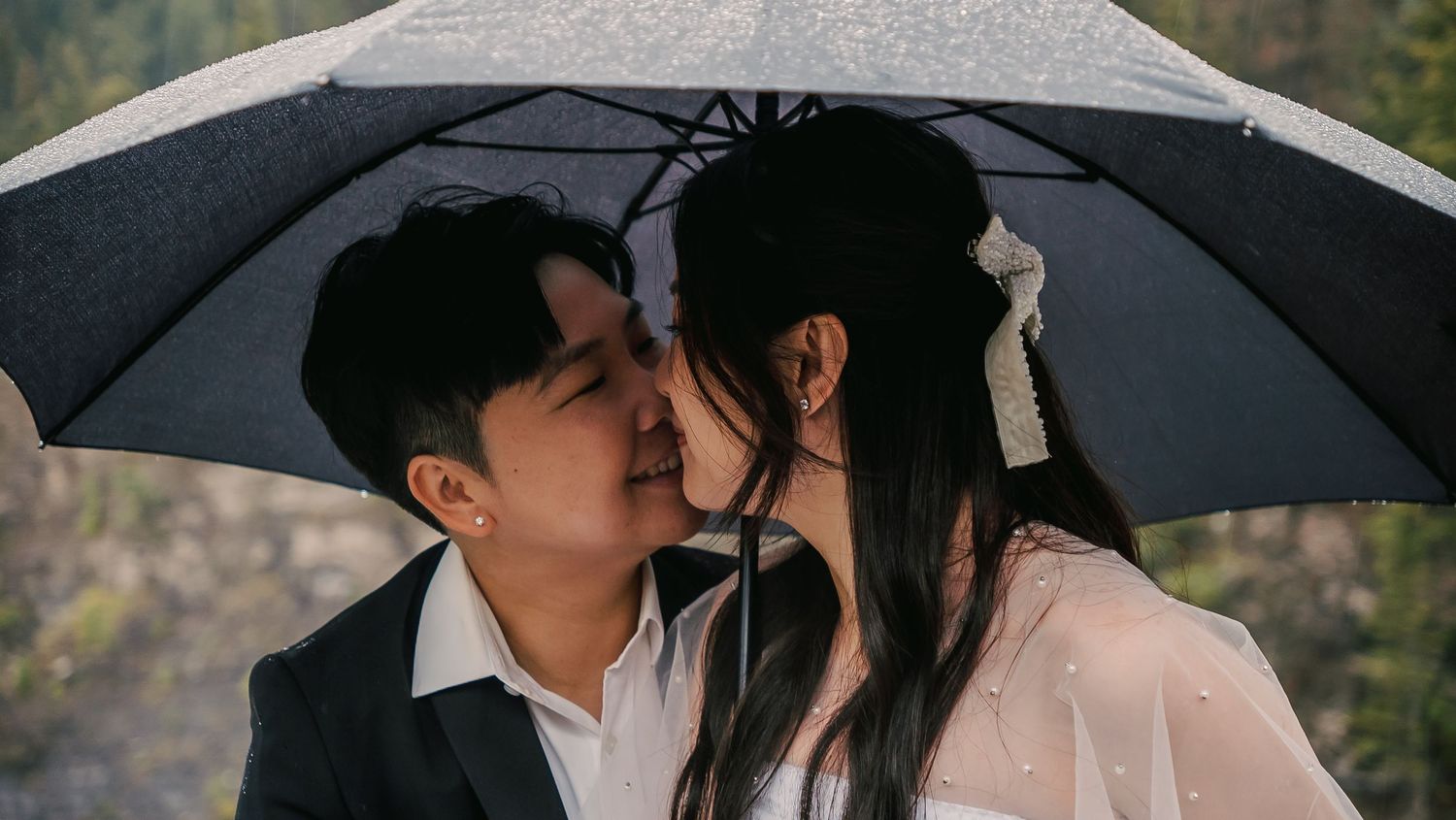 Couple sharing intimate moments under black umbrellas in a romantic outdoor photoshoot.