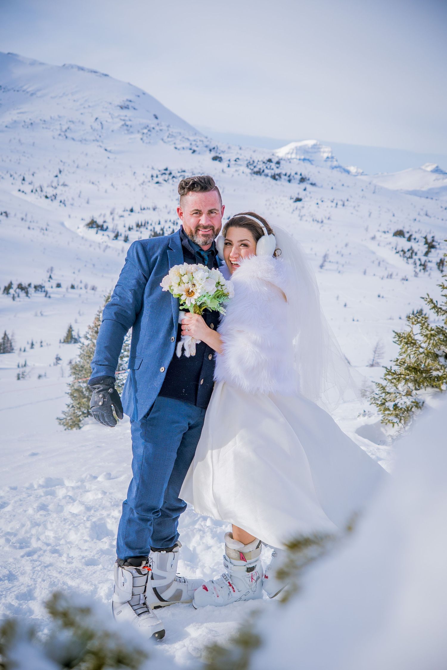 A winter wedding scene with a couple posing in snowy mountains wearing formal attire and warm white outerwear.