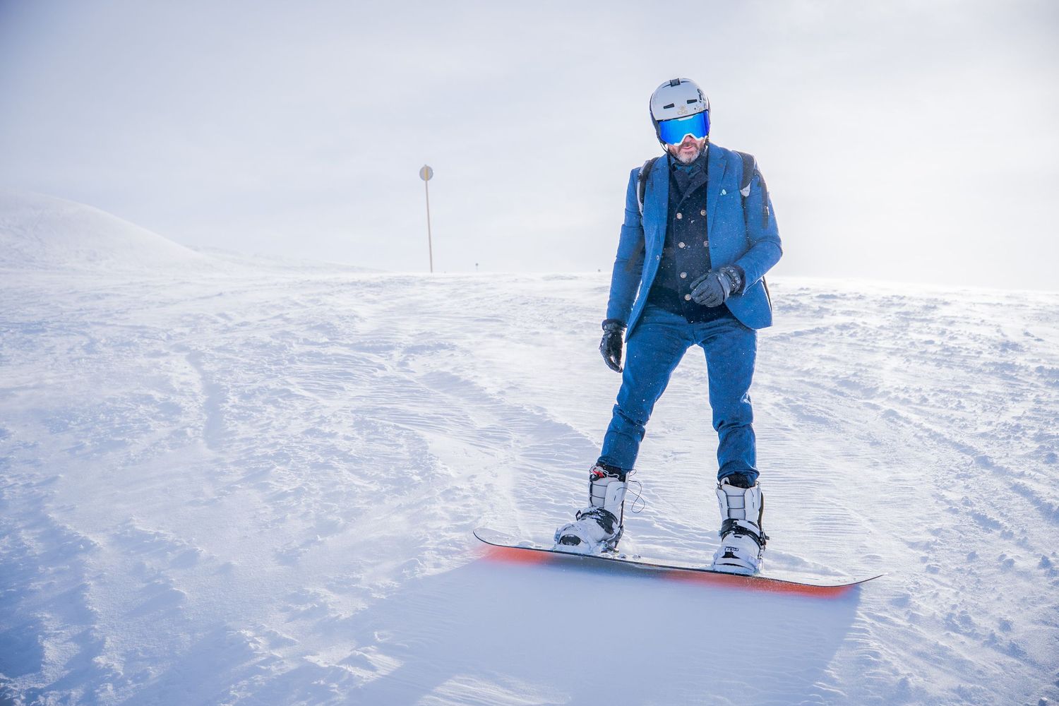 A snowboarder in bright blue winter gear performs a series of turns down a snowy slope on a clear day.