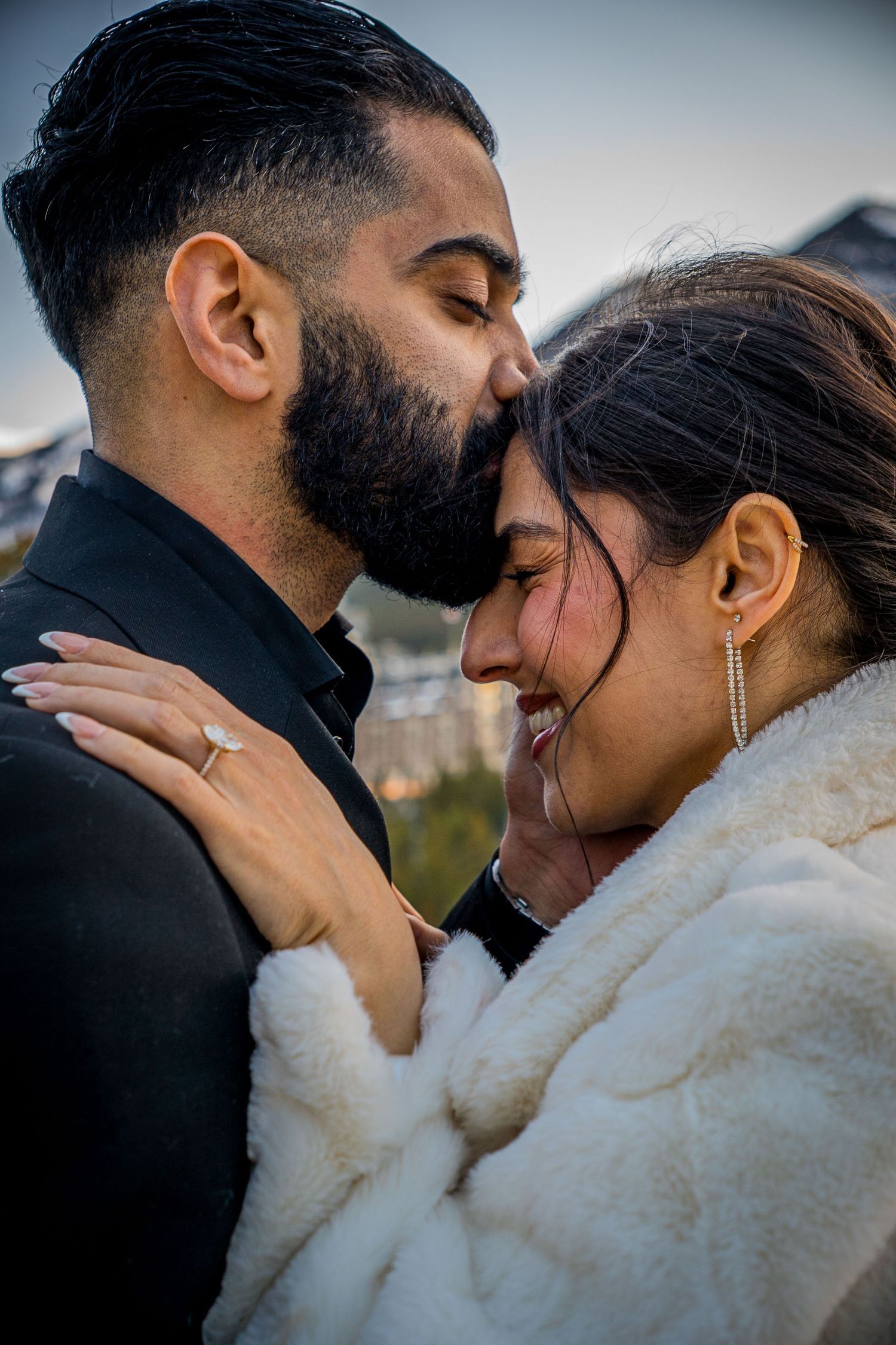 A romantic couple shares an intimate moment outdoors, with the person in white fur embracing their partner in black attire.