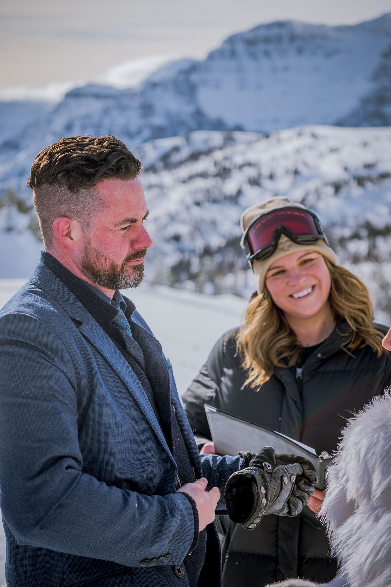 Two winter sports enthusiasts share a moment against a snowy mountain backdrop in ski gear and winter attire.