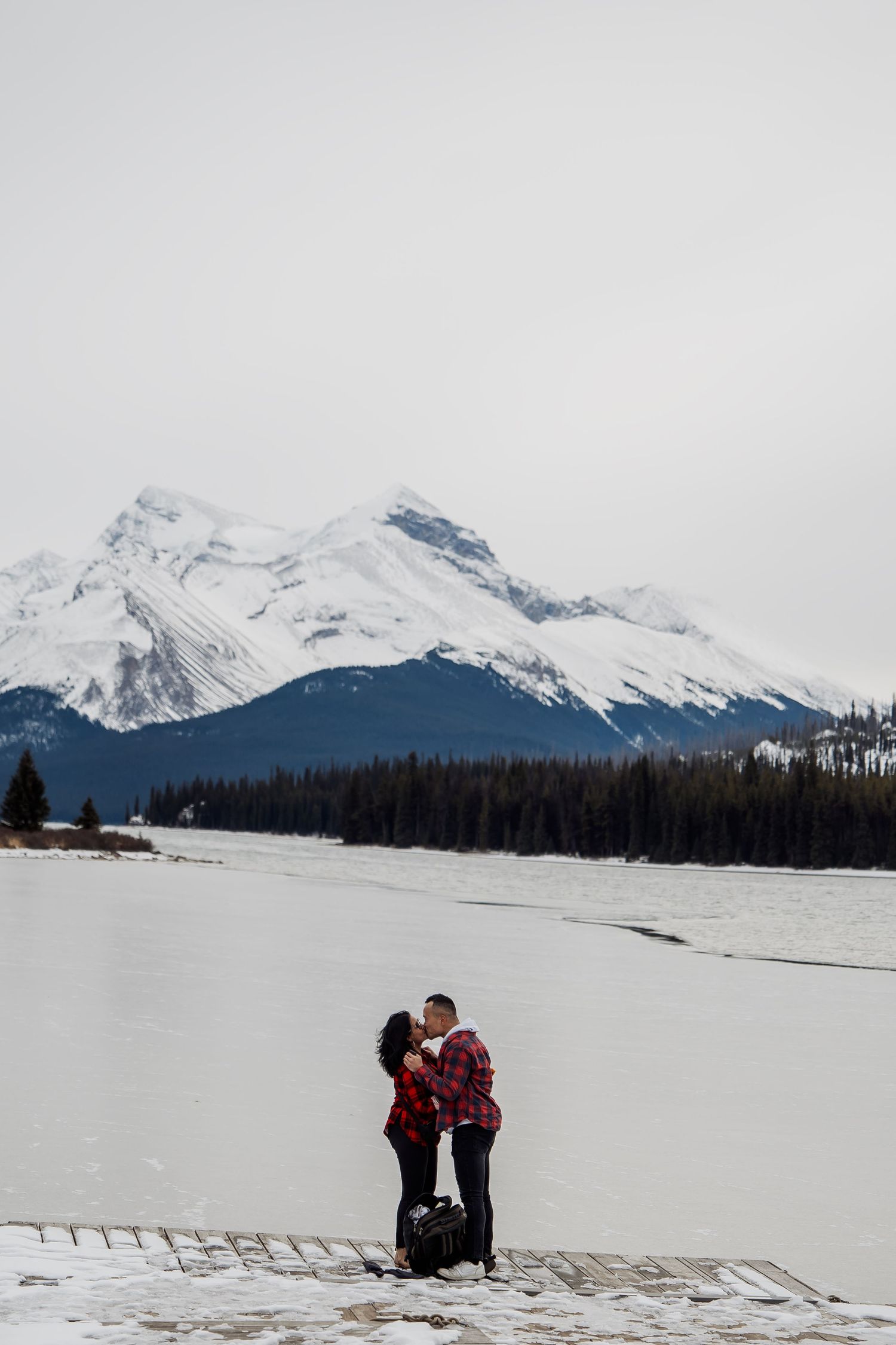 A couple in matching red plaid embraces in a snowy mountain landscape.
