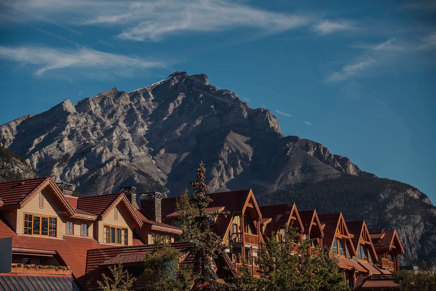Row of wooden mountain lodges nestled beneath towering rocky peaks with blue sky overhead in Banff National Park.