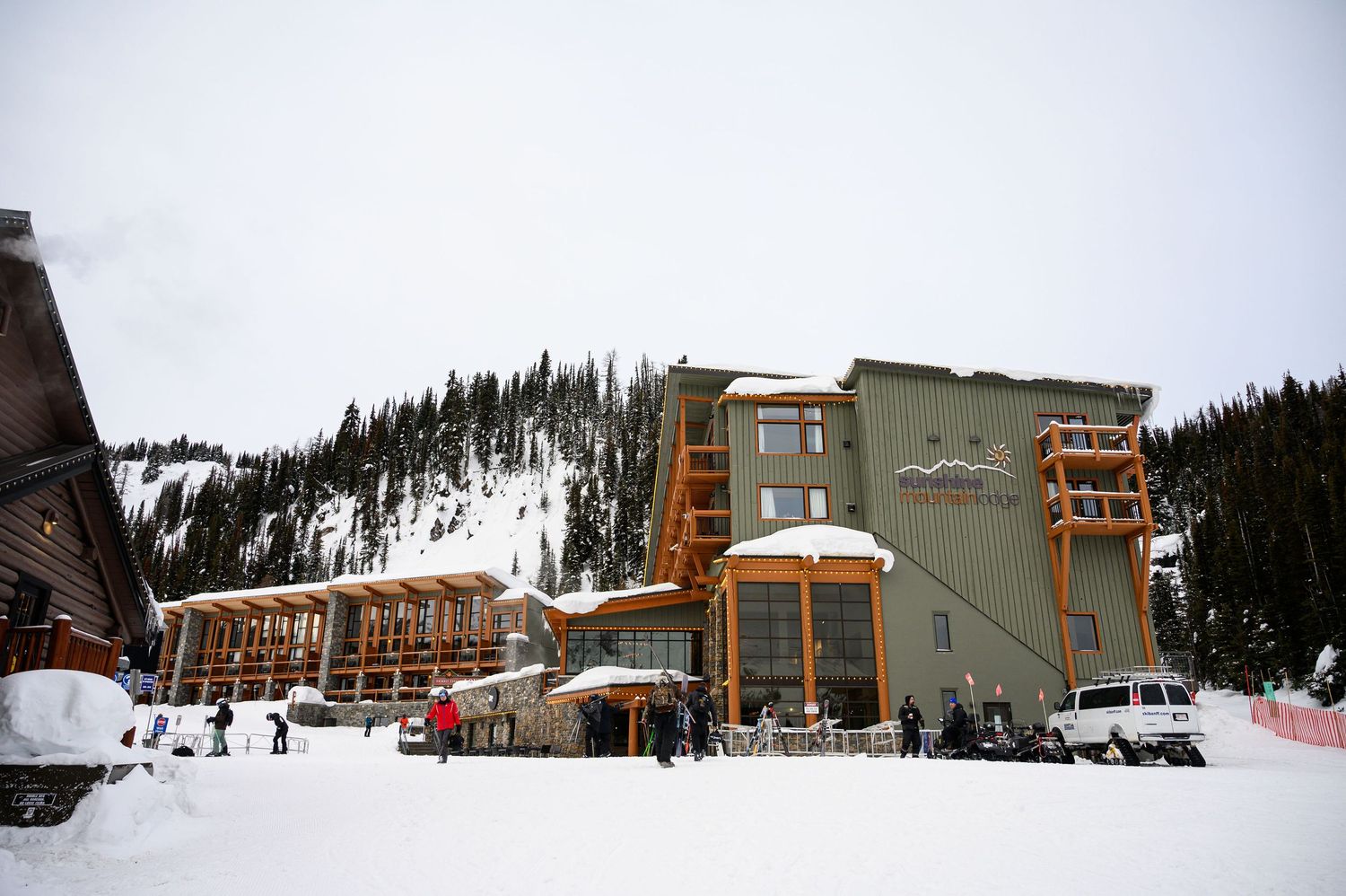 Panoramic view of a snow-covered ski resort with wooden lodge buildings and ski lifts against a cloudy mountain backdrop.