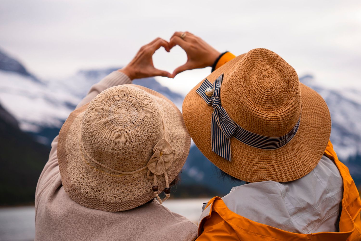 Two straw hats rest on a wooden railing with a scenic mountain lake view in the background.