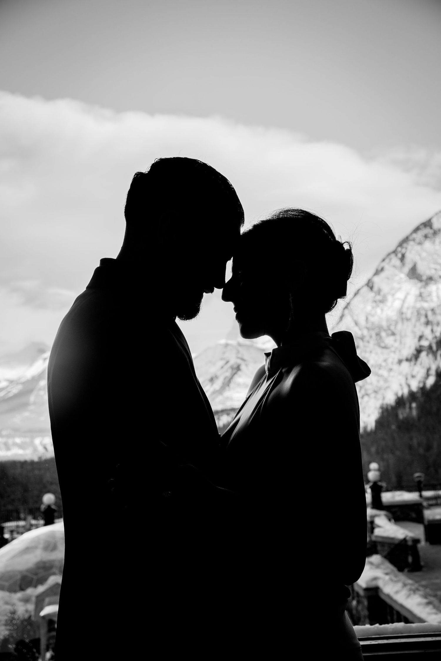 A silhouetted couple embraces against a mountain backdrop in a romantic black and white photo series.