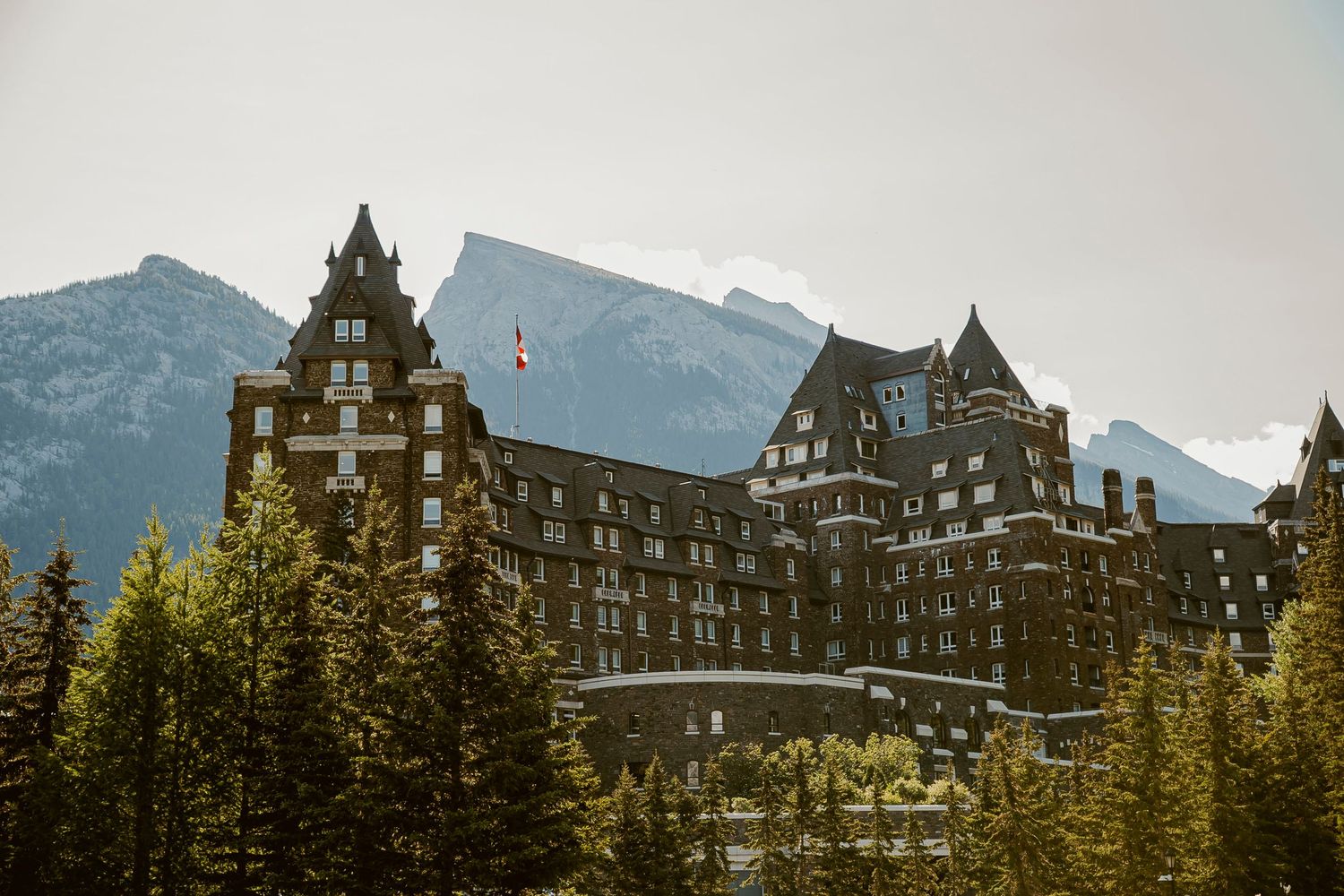 A panoramic view of the historic Fairmont Banff Springs Hotel nestled in the Canadian Rocky Mountains against a cloudy sky.