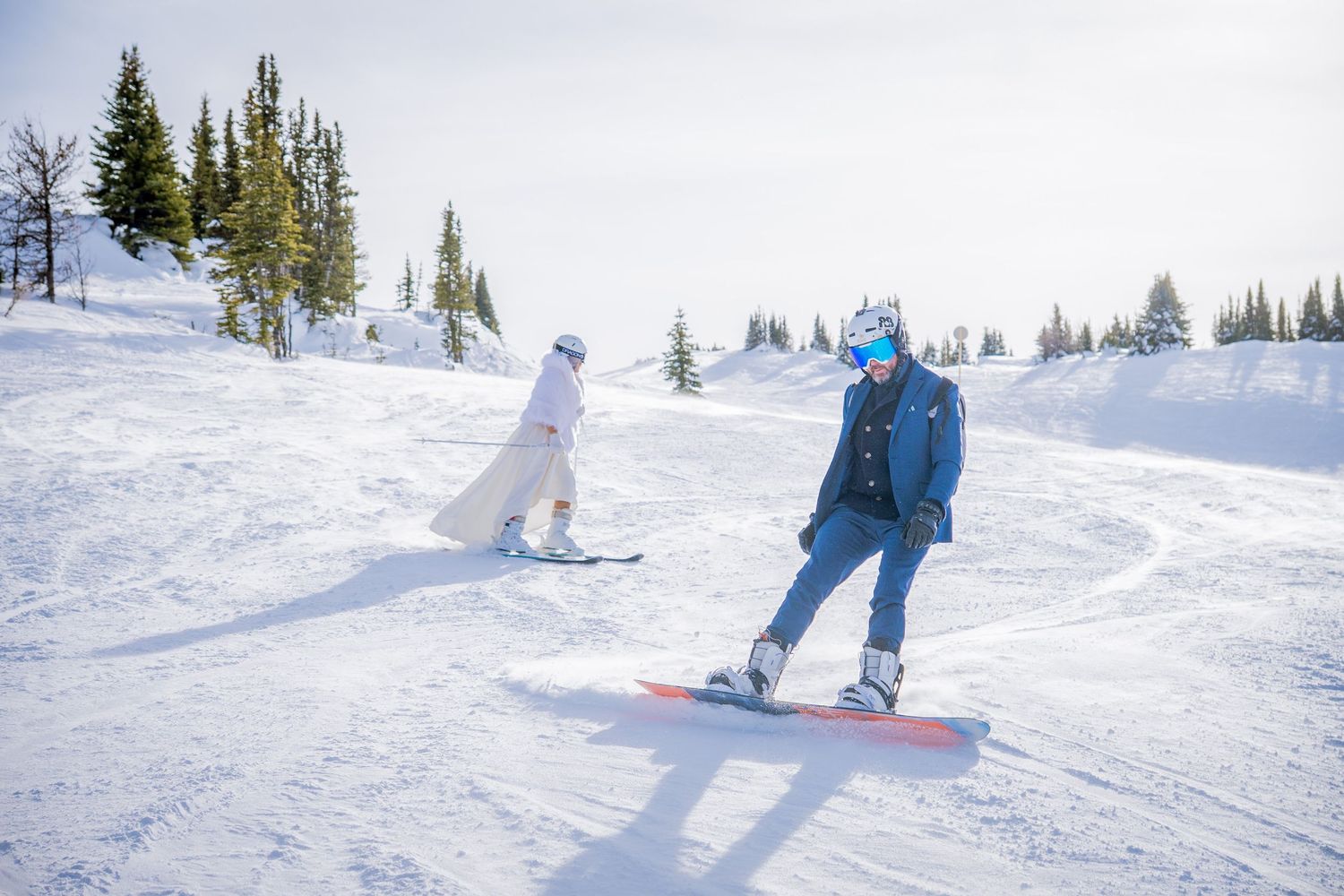 Skiers and snowboarders glide down a snowy mountain slope on a bright winter day.