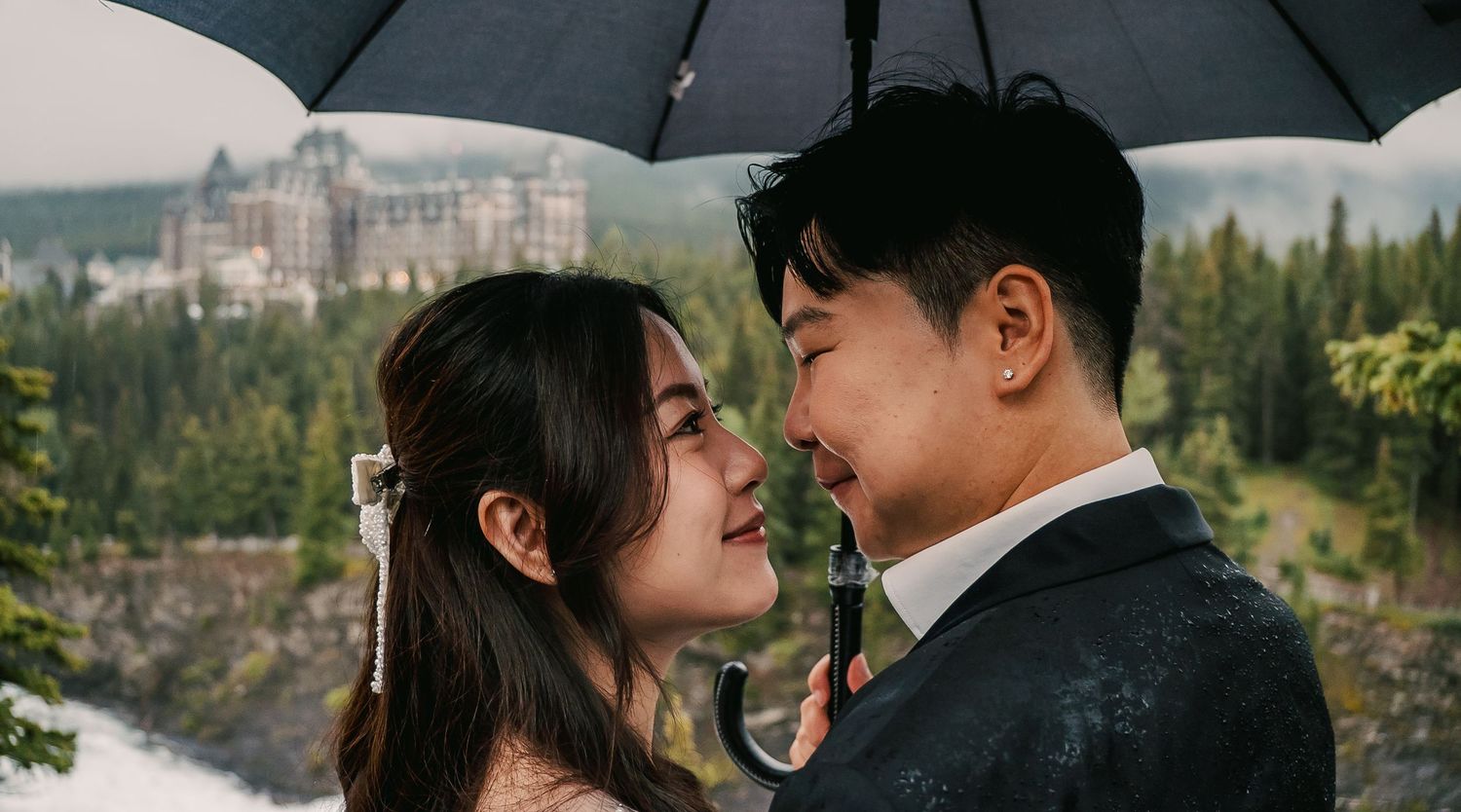 Romantic couple sharing an intimate moment under a black umbrella against a mountain backdrop.