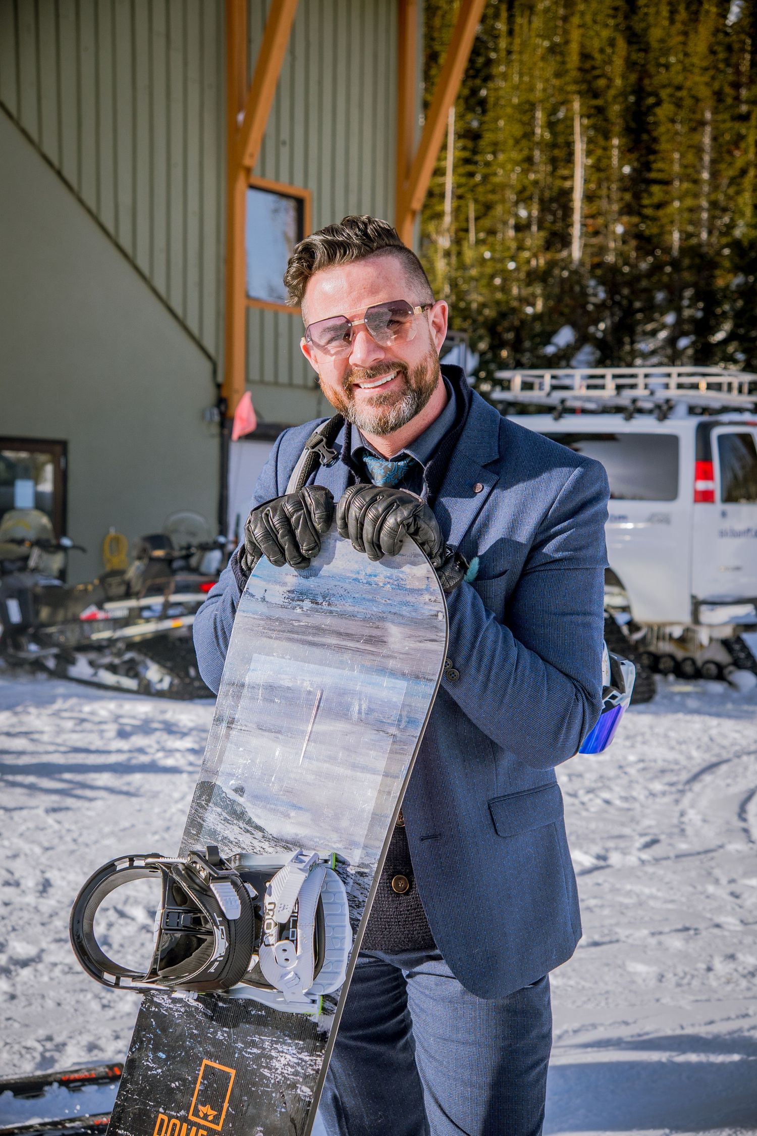 A person in a navy suit jacket displays an ice block containing frozen objects in a snowy outdoor setting.
