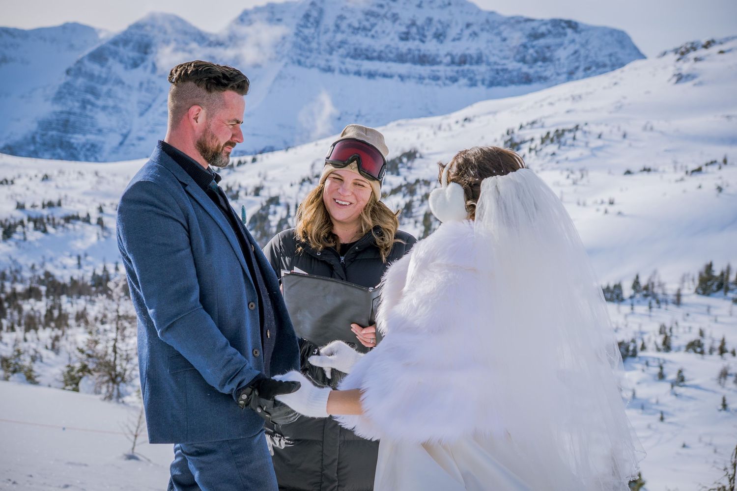 A winter mountain wedding ceremony takes place with snow-capped peaks in the background.