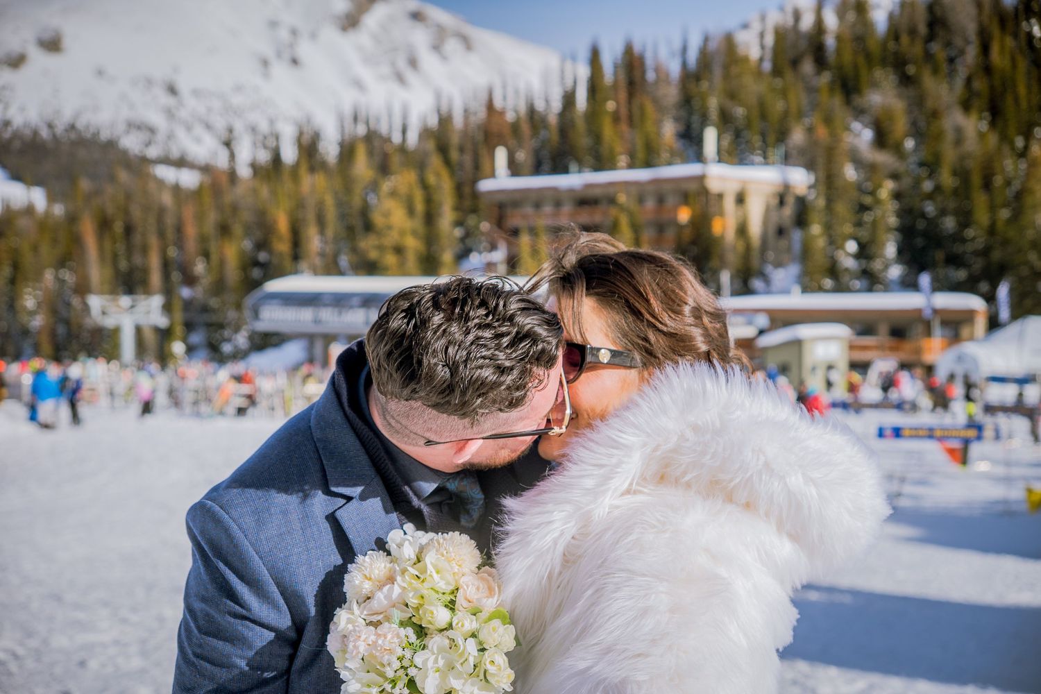 A winter wedding couple shares a romantic moment in the snowy mountains with evergreen trees in the background.