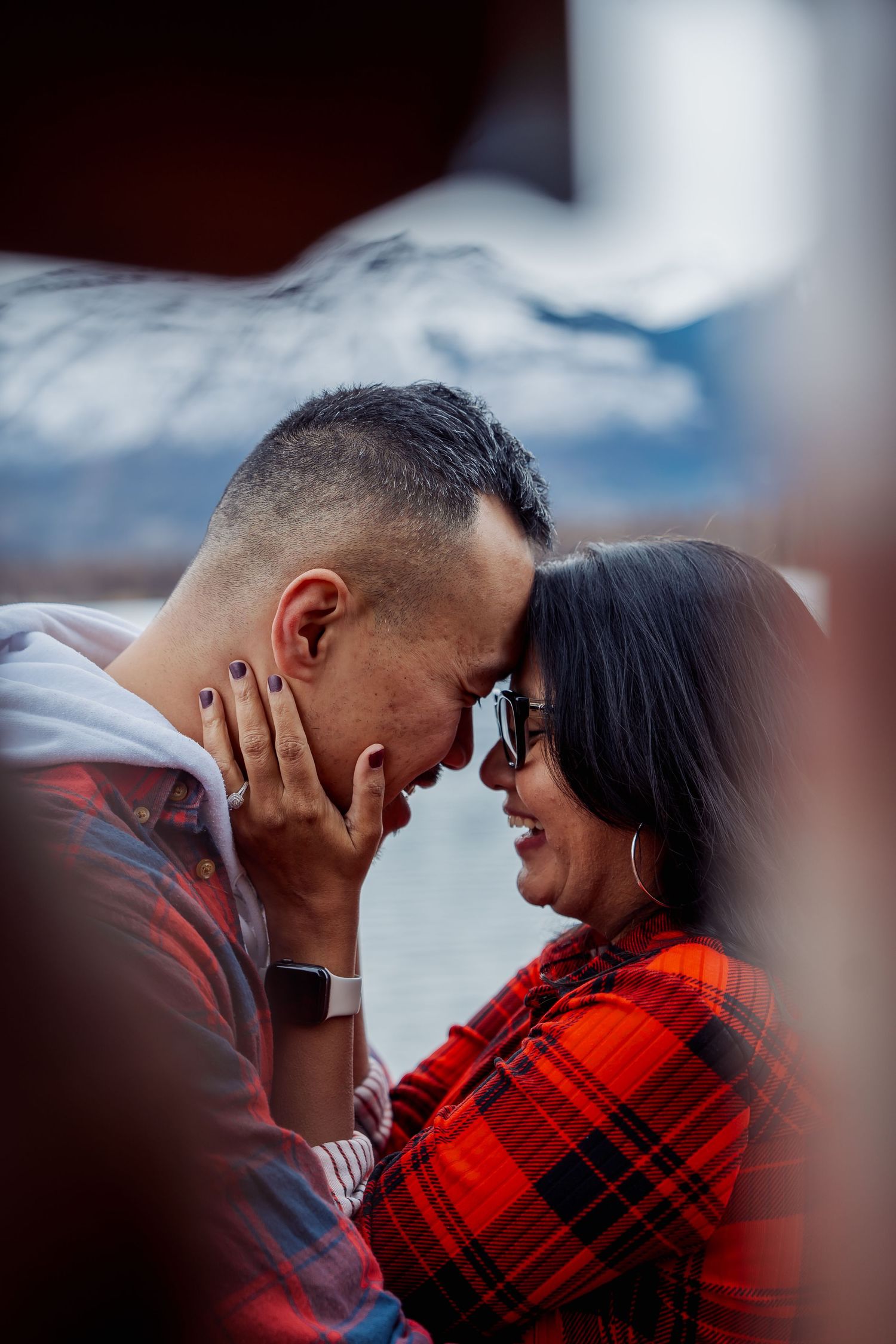 An intimate moment between a couple wearing casual attire against a mountain backdrop.