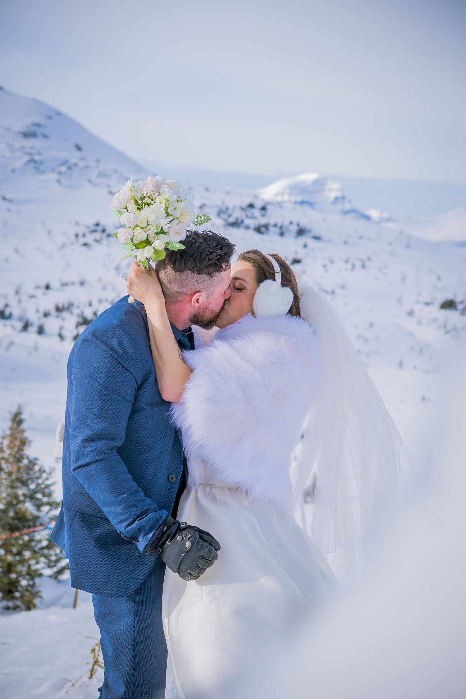 A romantic winter wedding moment captured in the snowy mountains with snow-capped peaks in the background.