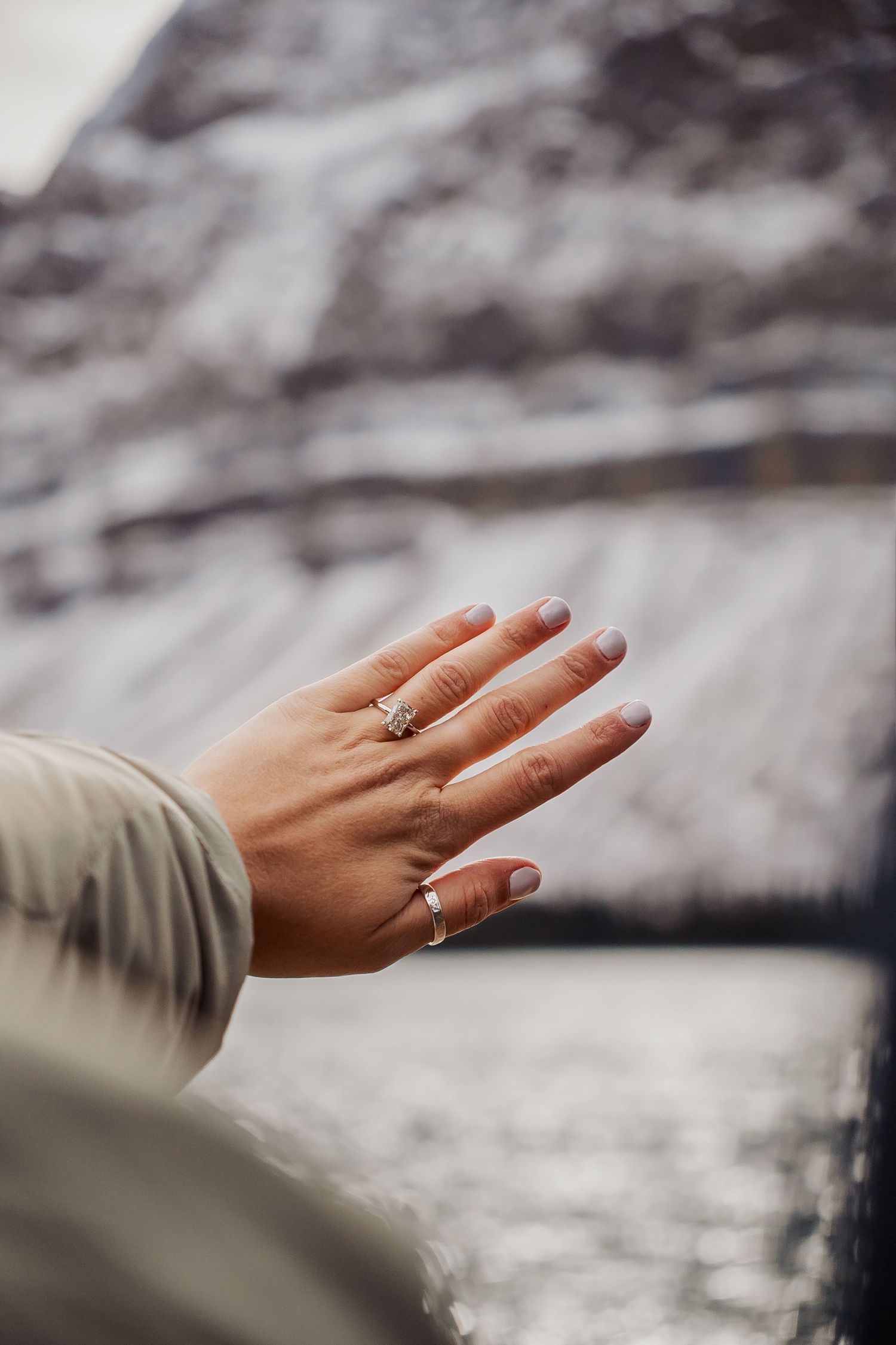 A hand wearing multiple delicate rings reaches out against a blurred winter background.