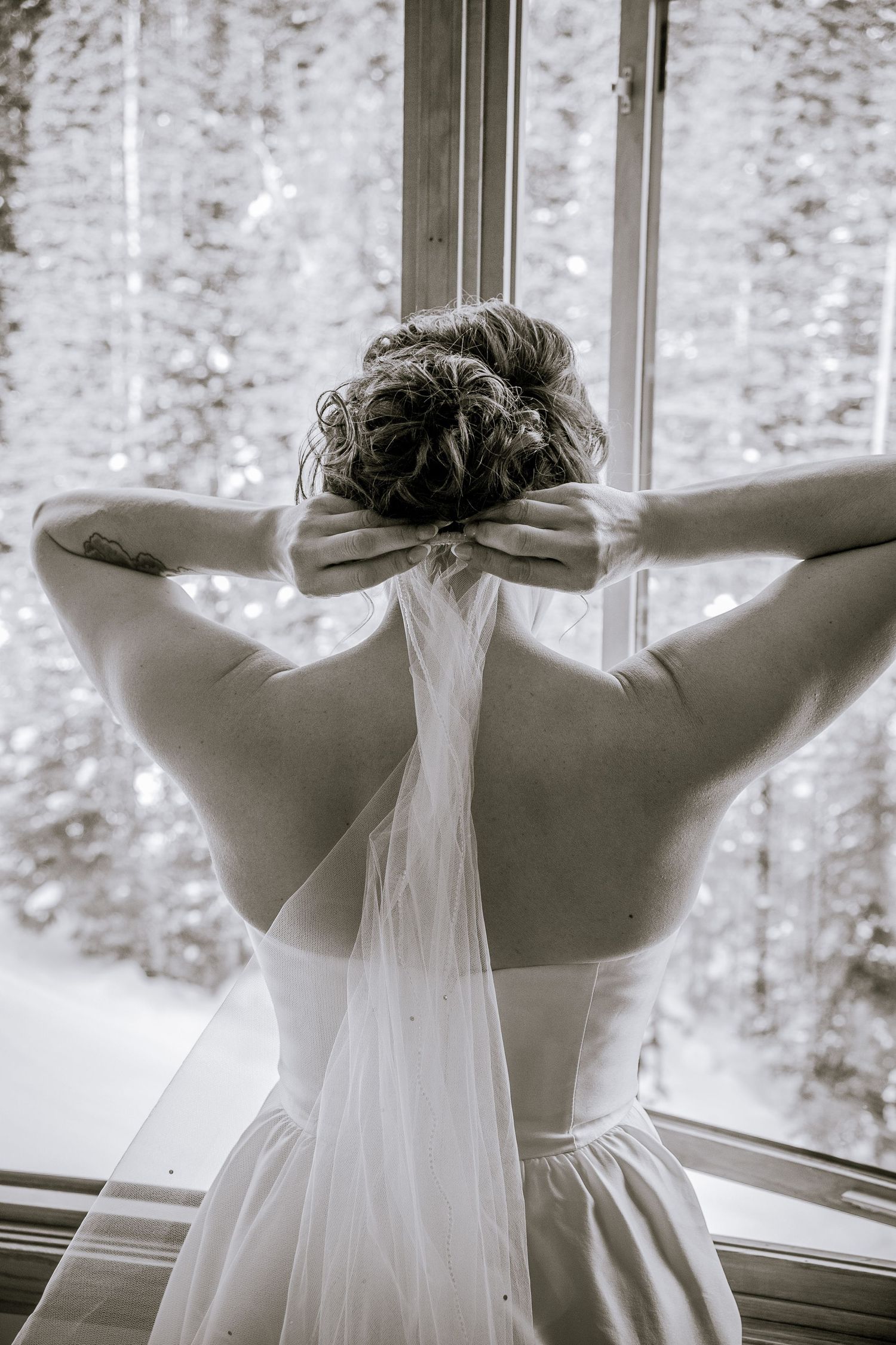 Back view of bride in white wedding dress looking out window with snowy landscape.
