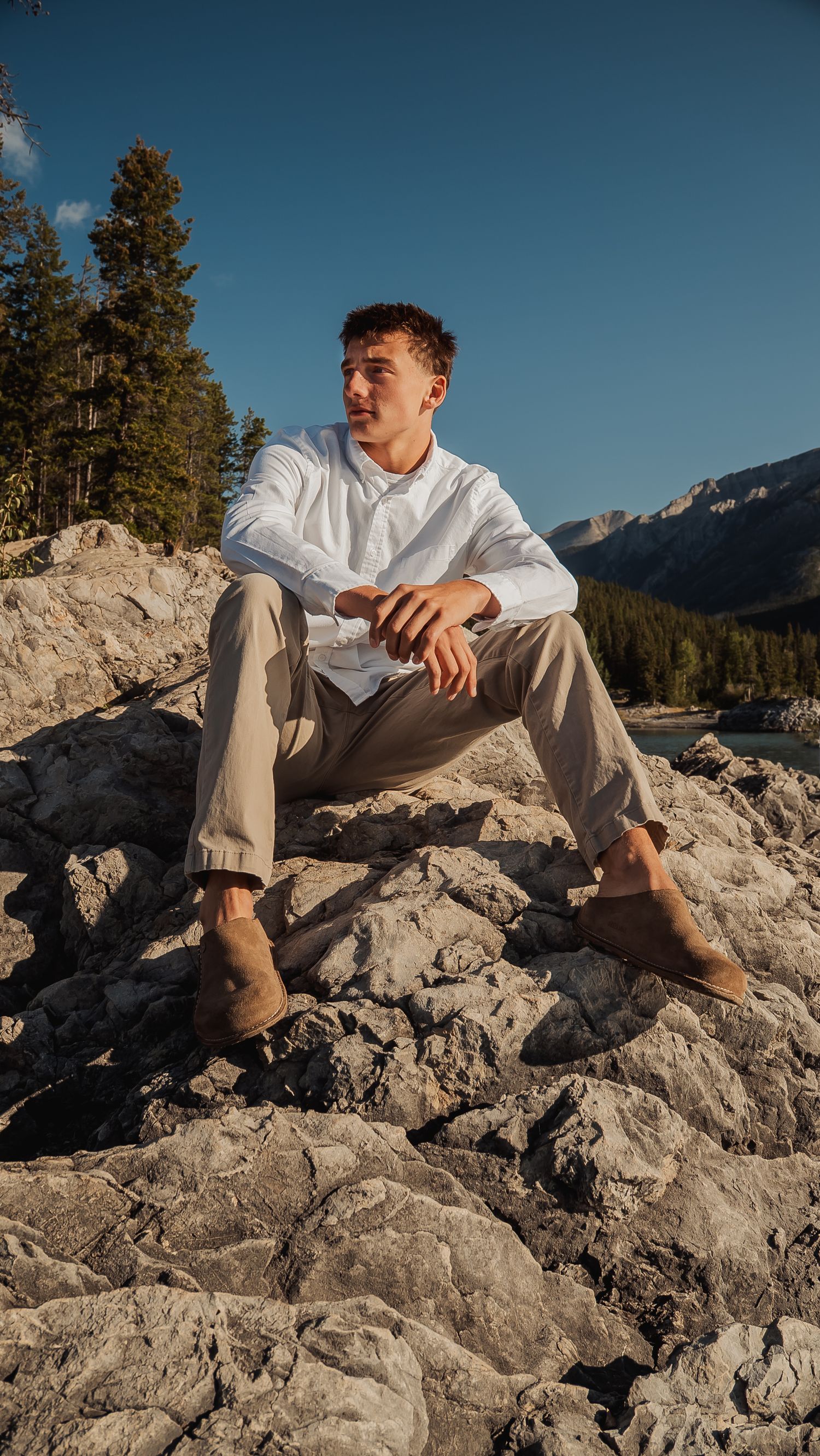 Person in casual attire relaxing on rocky mountain ledge with scenic mountain backdrop.