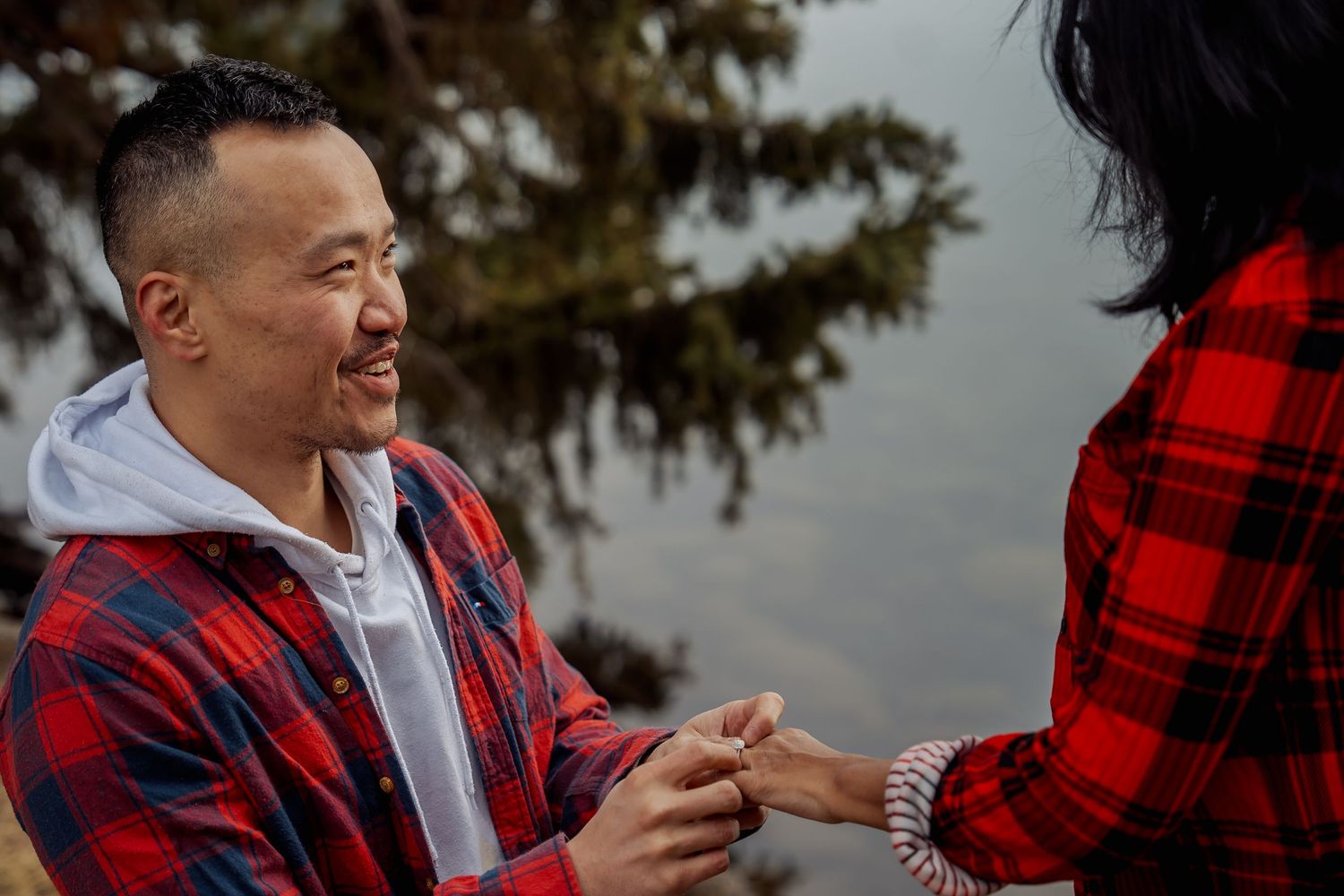 Couple in red plaid flannel shirts sharing an intimate moment against a mountain backdrop.