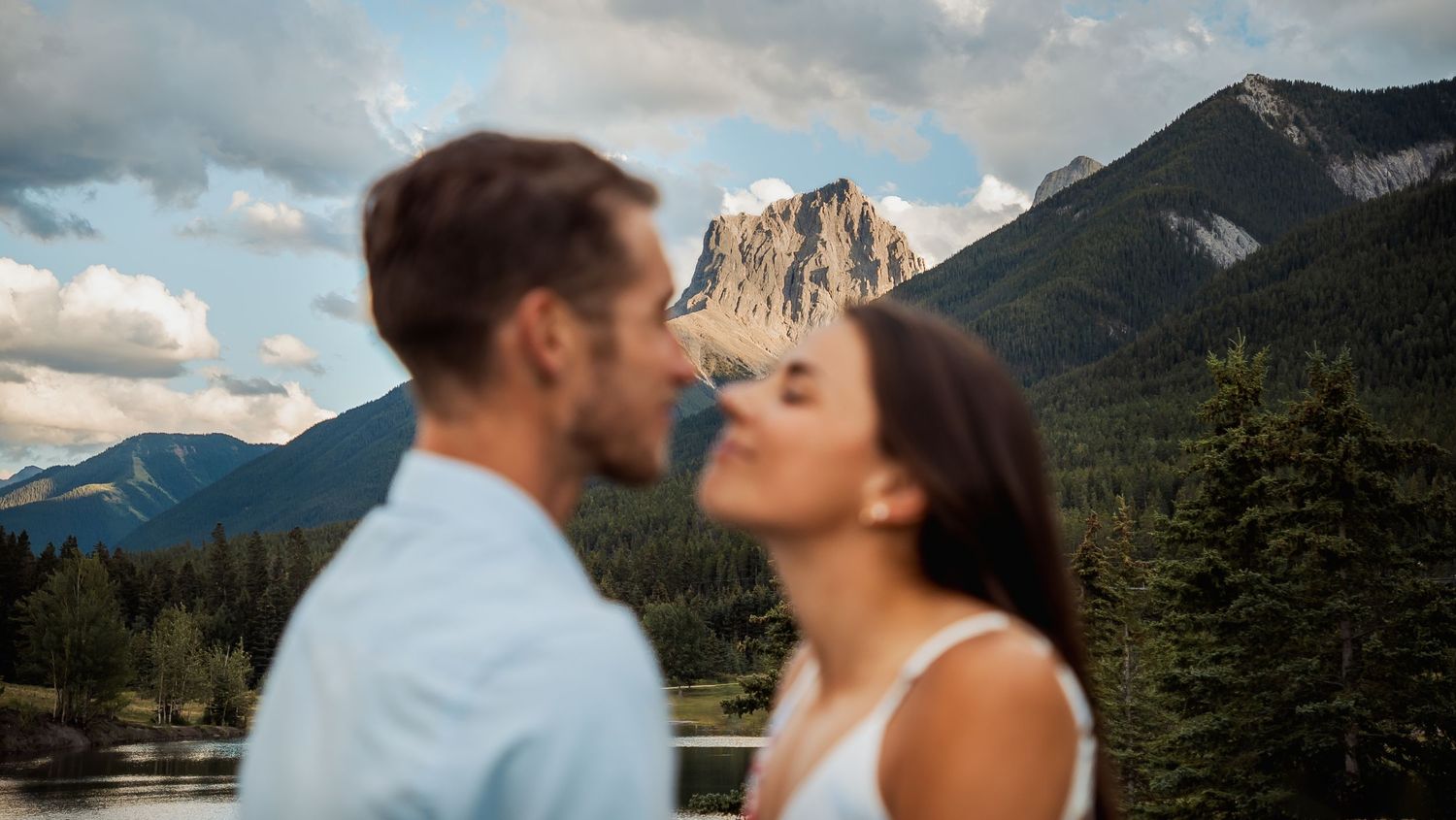 A romantic couple shares tender moments against a backdrop of mountain peaks and cloudy skies.