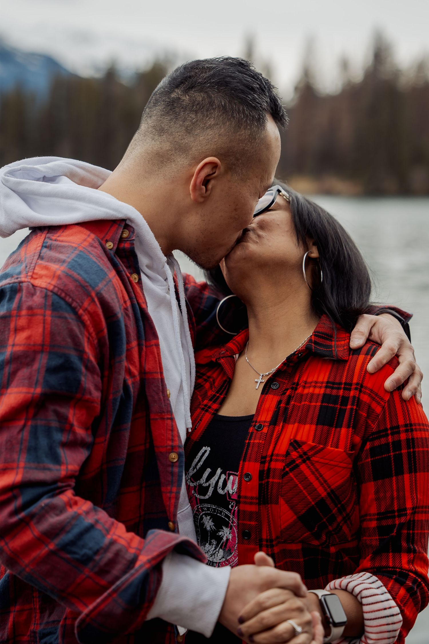 Couple in red plaid and black outfits sharing intimate moments outdoors by a lake in a series of romantic photos.