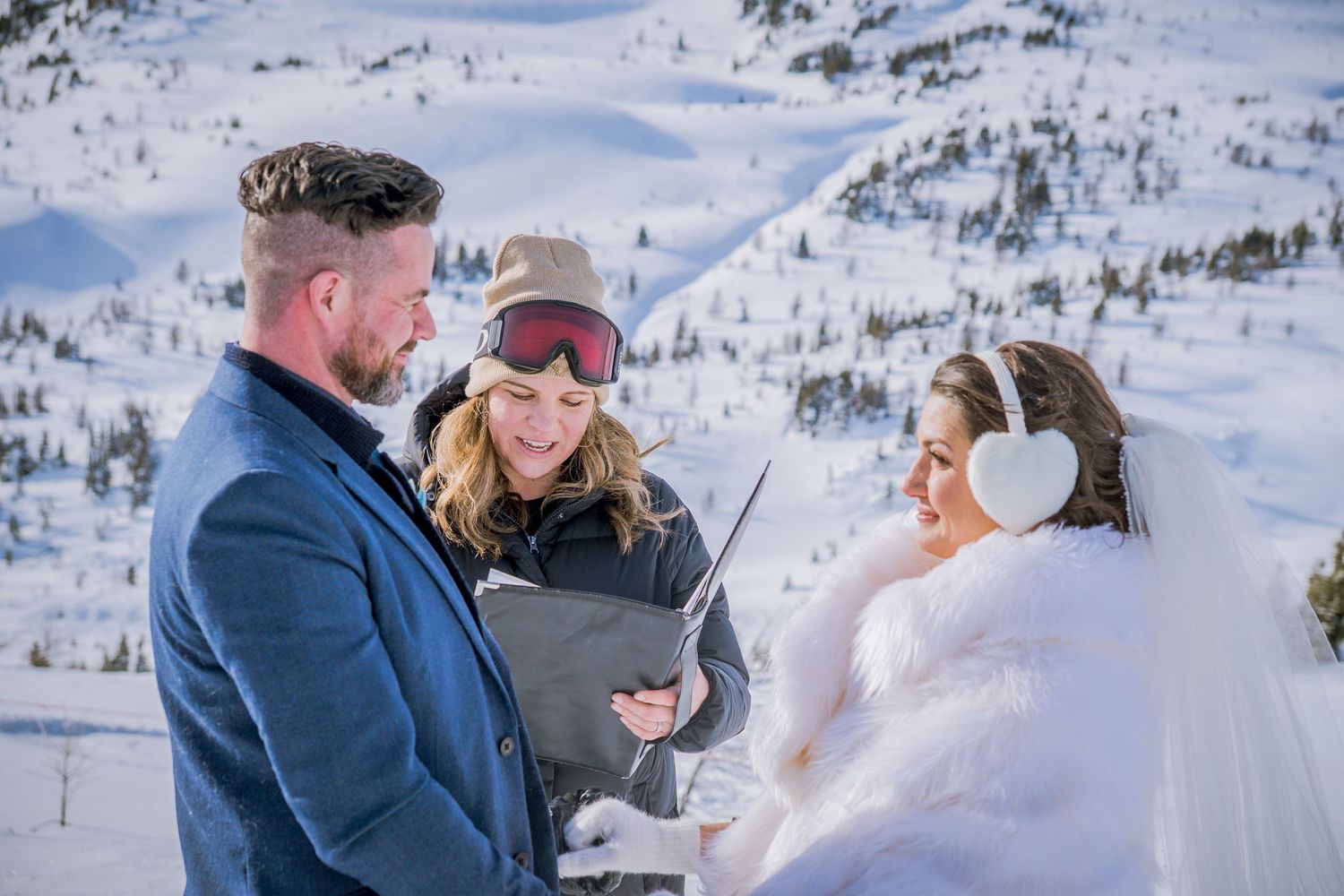 Winter mountain wedding ceremony with snow-covered peaks and blue skies in the background.