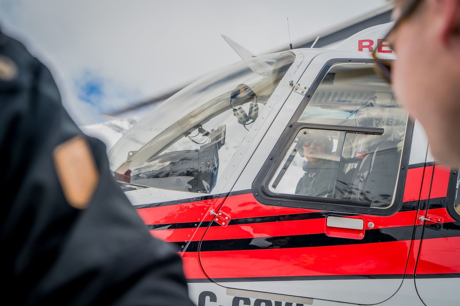 Close-up view of a red and white rescue helicopter cockpit with an officer standing nearby.