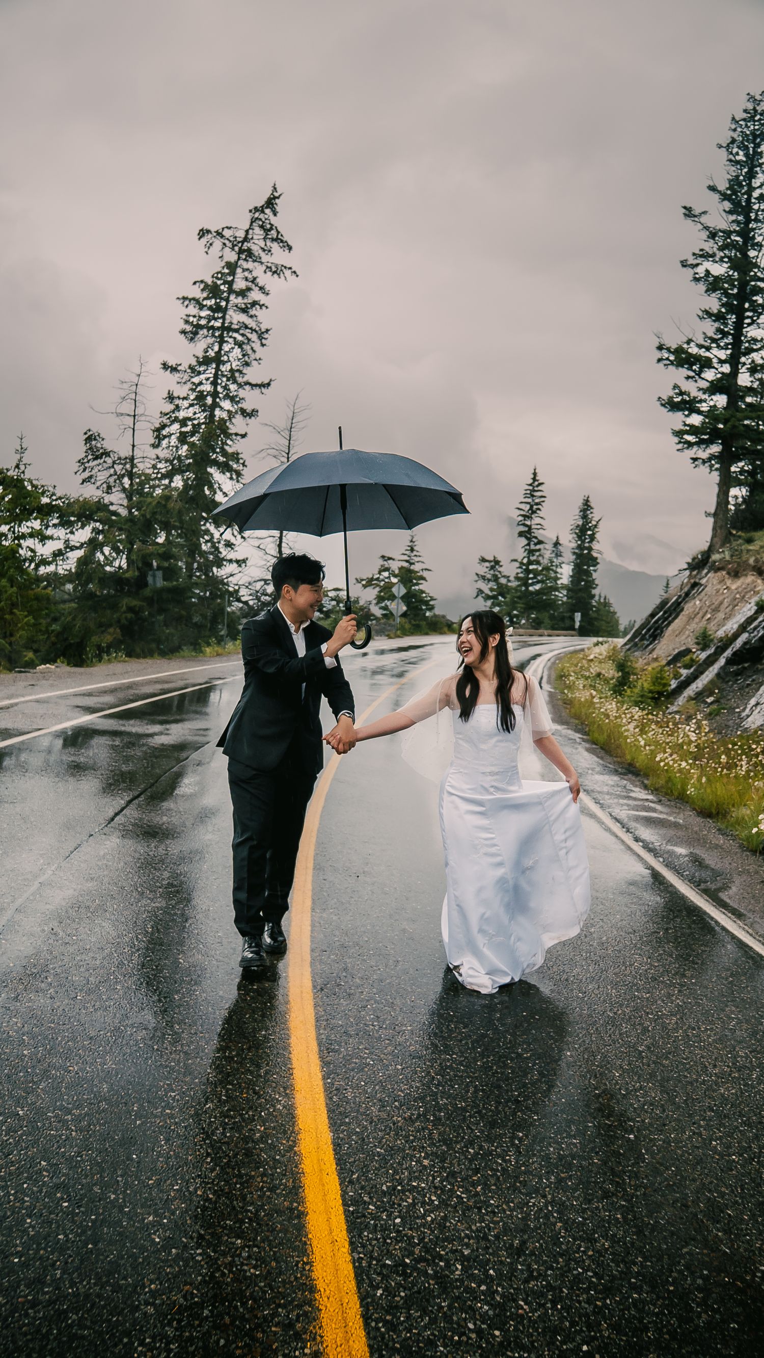 A couple shares umbrellas on a rainy mountain road while wearing formal attire in a romantic photo sequence.