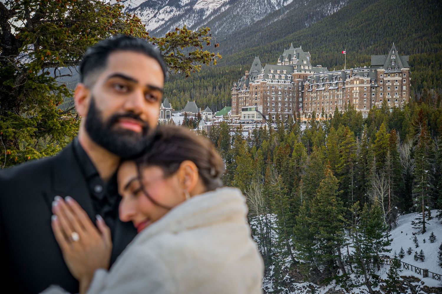 A romantic winter engagement photoshoot with snowy mountains and the Fairmont Banff Springs Hotel in the background.