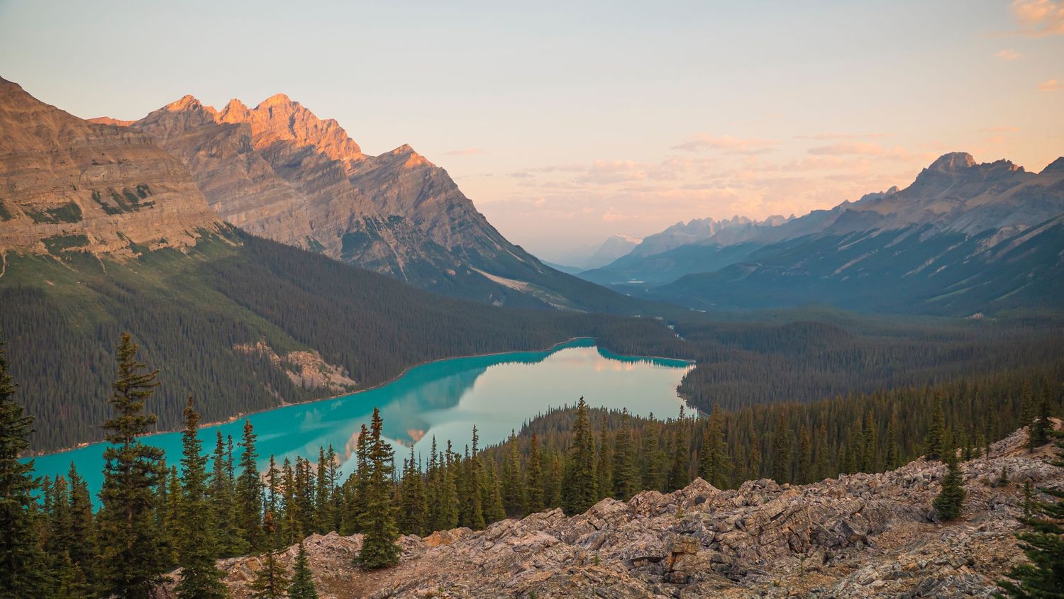 Panoramic view of turquoise lakes and mountain ranges in Canadian Rockies during golden hour.