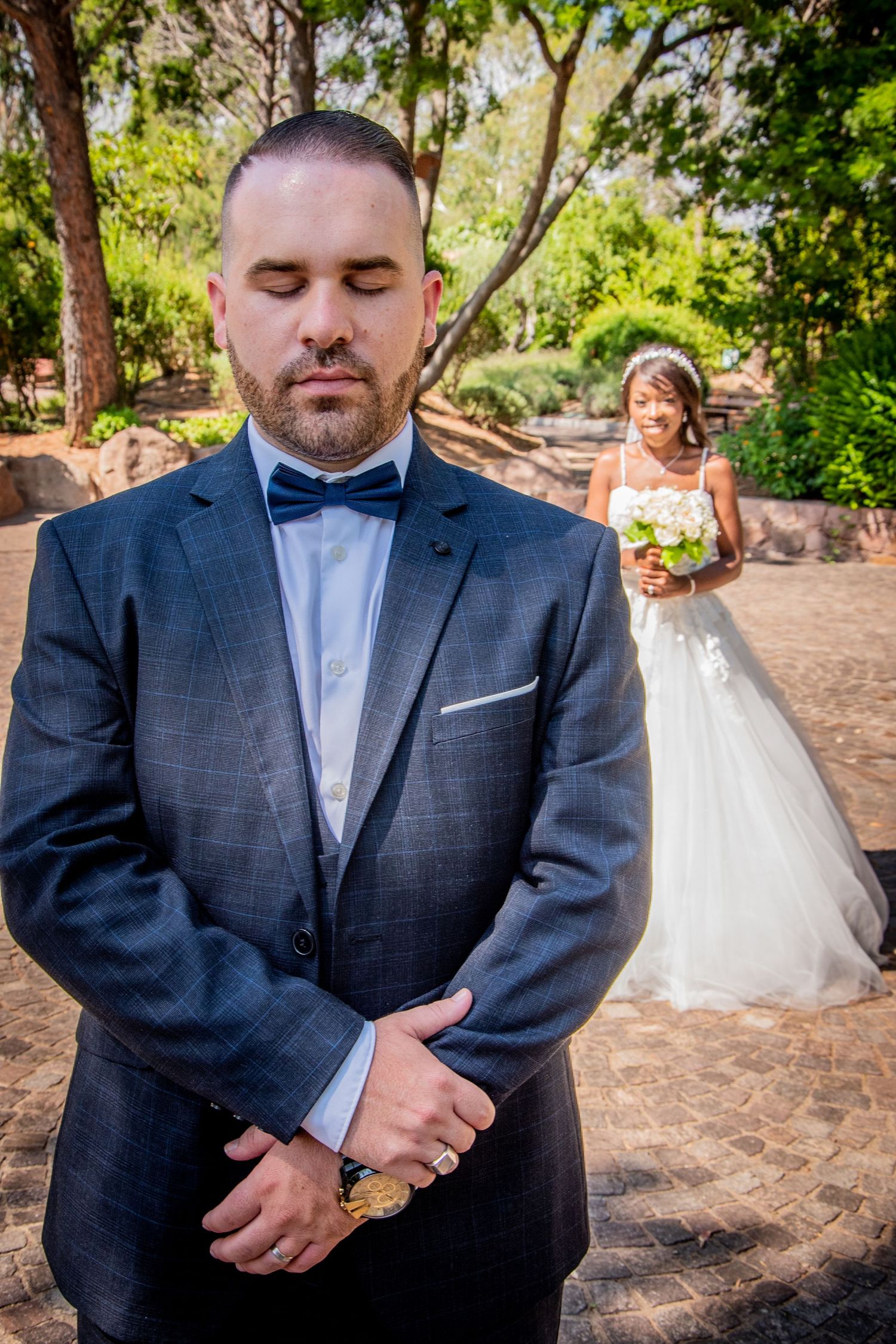 A series of wedding photos showing a groom in a navy suit and blue tie standing in an outdoor garden setting.