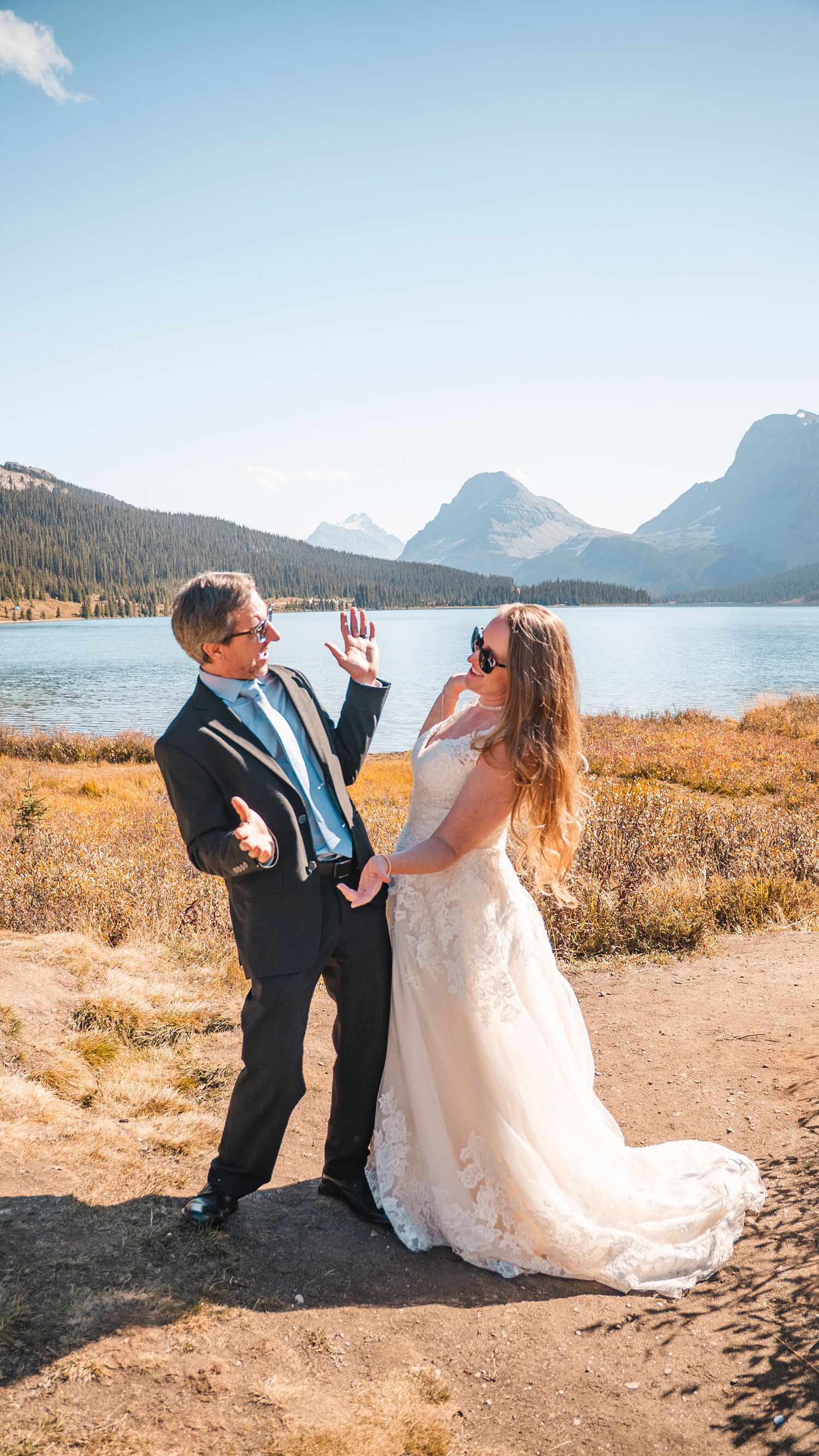 A playful wedding photo by a mountain lake with dramatic peaks in the background.