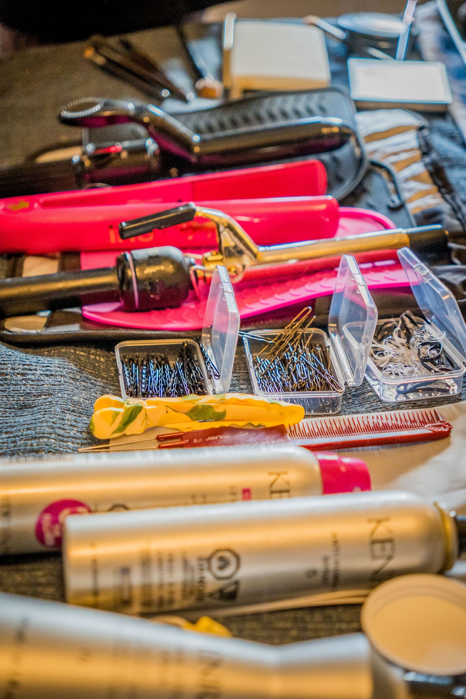 Hair styling tools including curling irons, bobby pins, combs, and hair products arranged on a salon work surface.