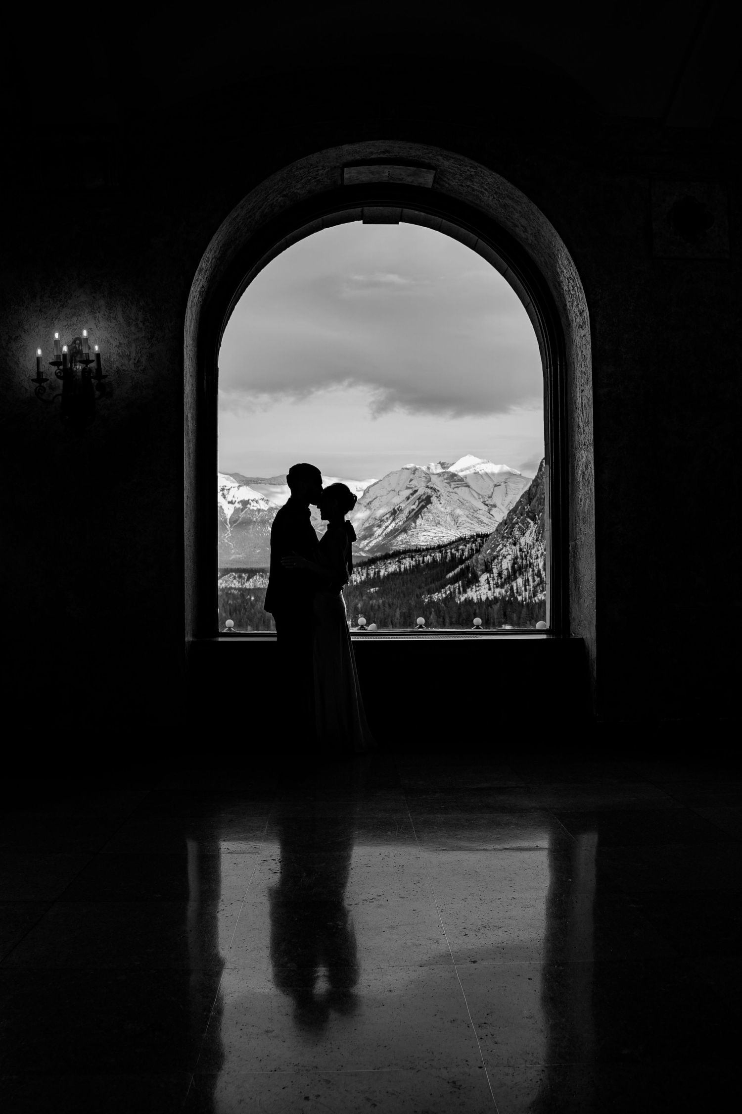 A silhouetted figure stands in an arched tunnel opening with snow-capped mountain peaks visible through the window.