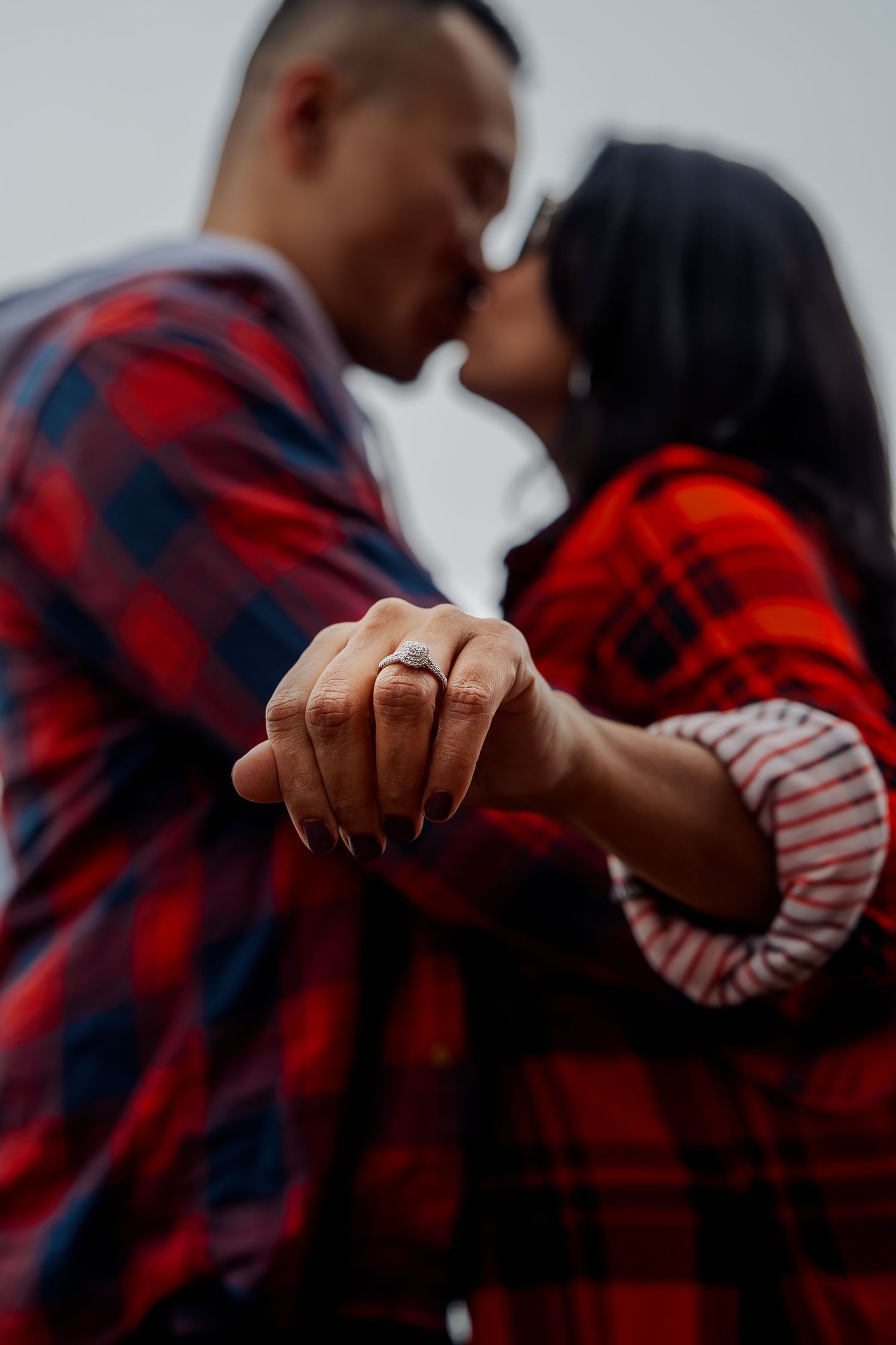 Close-up shot of hands wearing engagement rings against a blurred background.