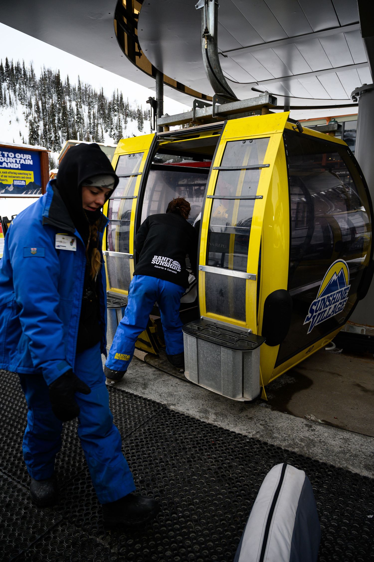 Person in blue ski jacket boarding a yellow gondola lift at a snowy mountain resort.