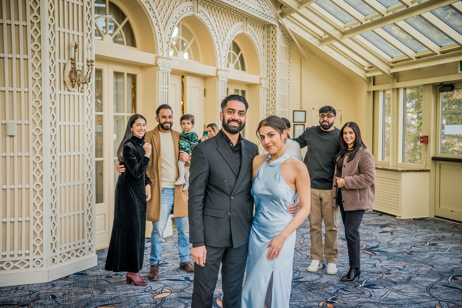 A group of people gather in an elegant hallway with ornate architectural details and a glass ceiling.