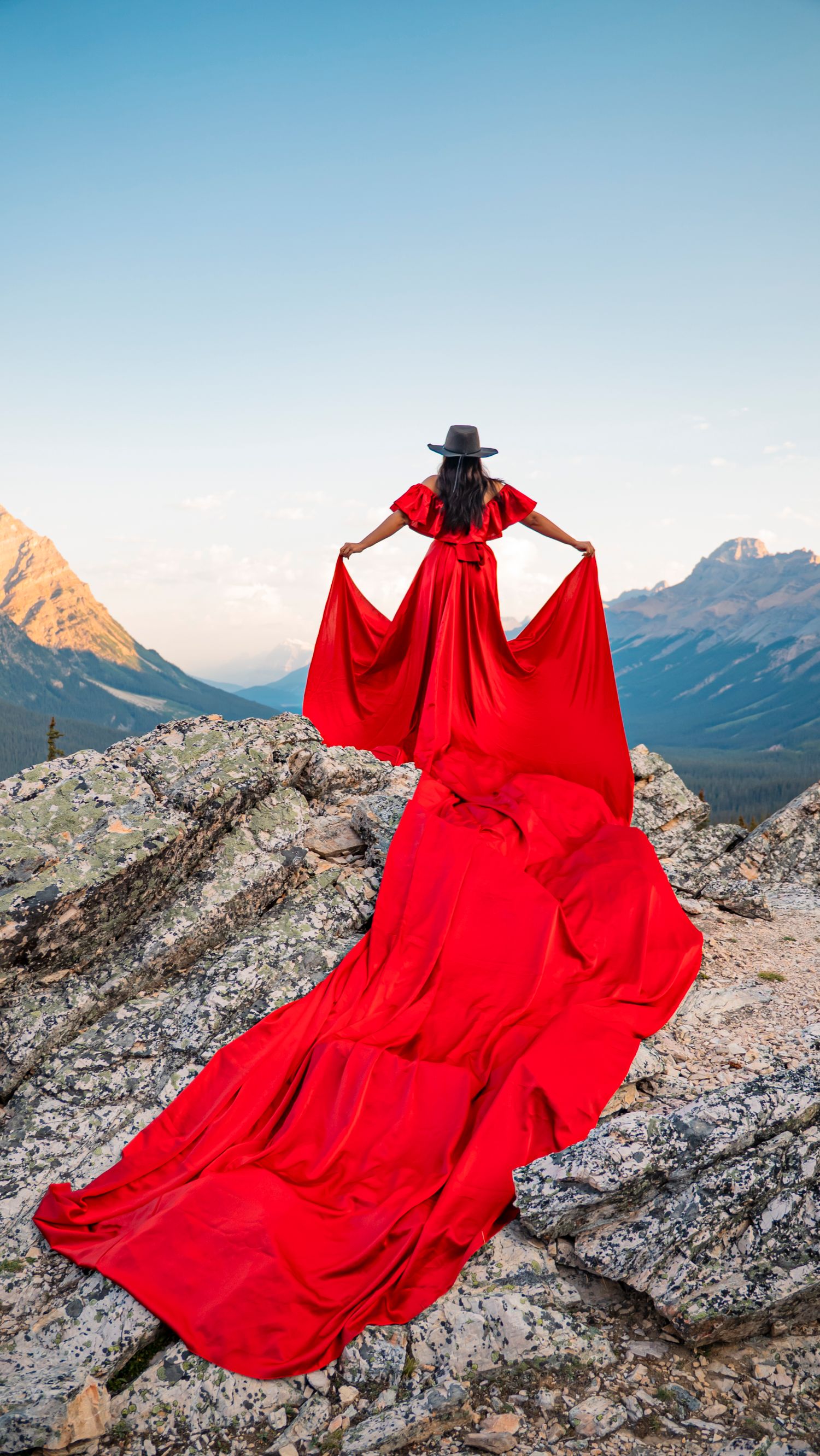 Flowing red dress billowing dramatically against rocky mountain peaks in dramatic outdoor photo series.