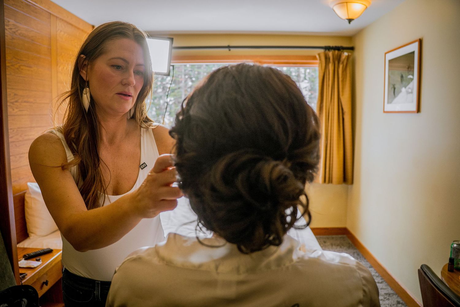 A bride gets ready for her wedding day in front of a mirror in a warmly lit room.