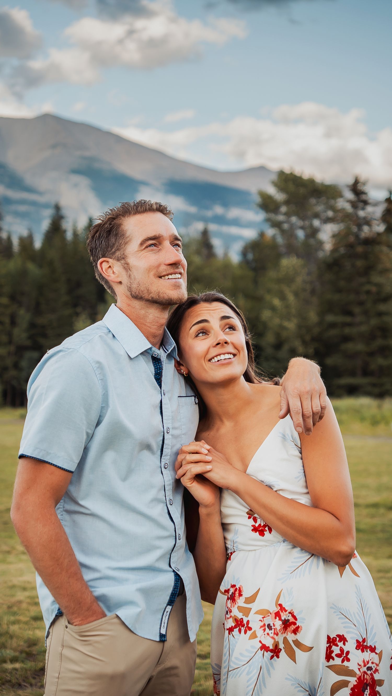 A couple shares a joyful moment together against a scenic mountain backdrop with evergreen trees.
