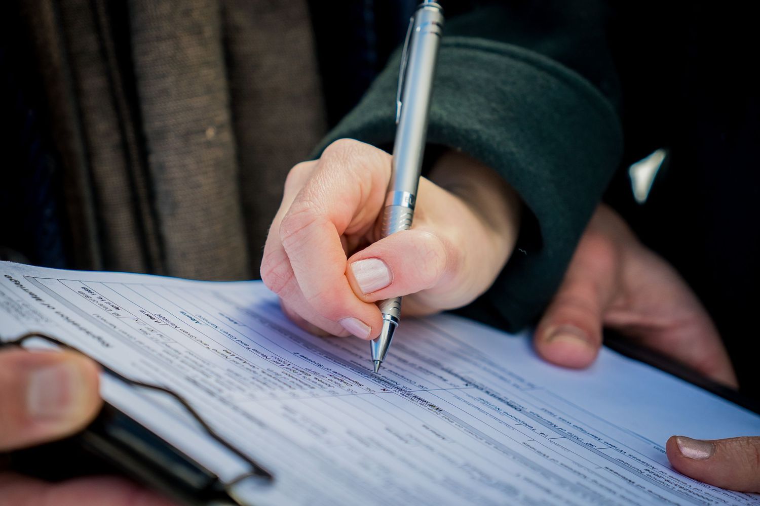 Close-up of a person signing an official document with a pen outdoors.