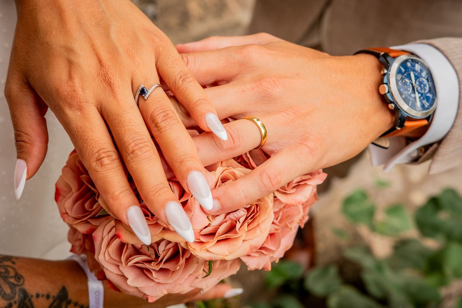 Close-up of hands exchanging rings during a wedding ceremony with pink rose petals in the background.