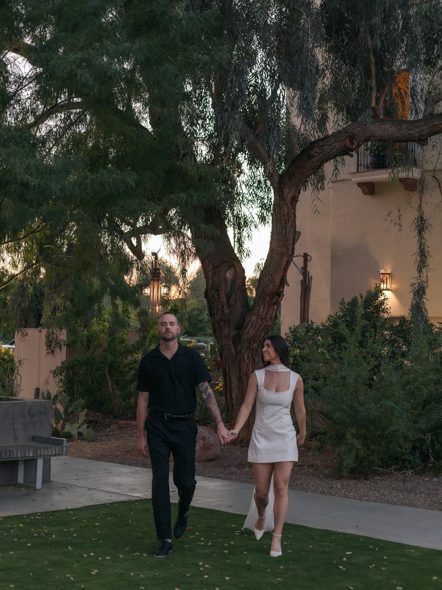 Couple walking hand in hand outside ivy covered building during engagement photoshoot with natural light photography