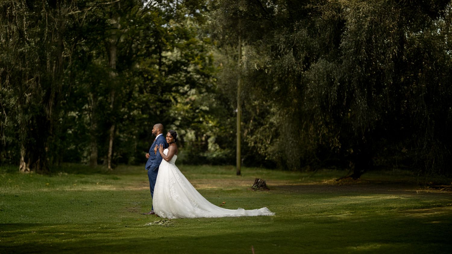 Romantic forest wedding portrait of bride in lace gown and groom in blue suit,captured in soft natural light by outdoor wedding photography