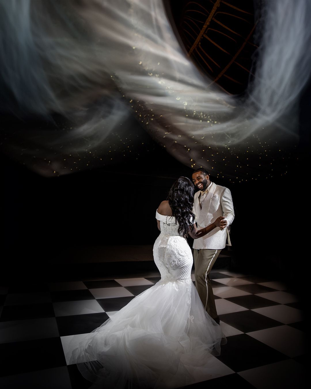 Romantic wedding scene, bride in white gown with long train, groom holding hands, dramatic light rays, dark artistic background, love moment