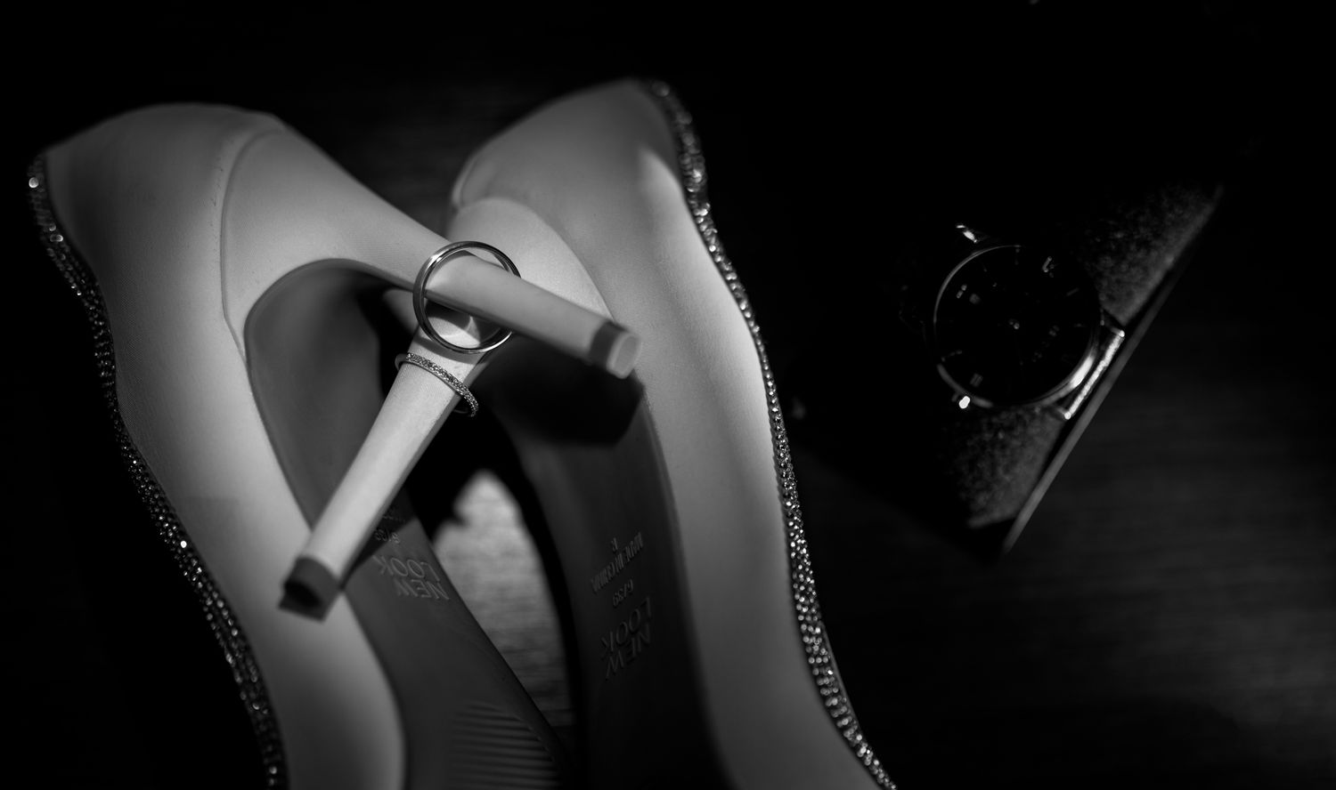Elegant black and white wedding detail photo featuring bridal heels, wedding rings, and groom’s watch, capturing timeless luxury and romance